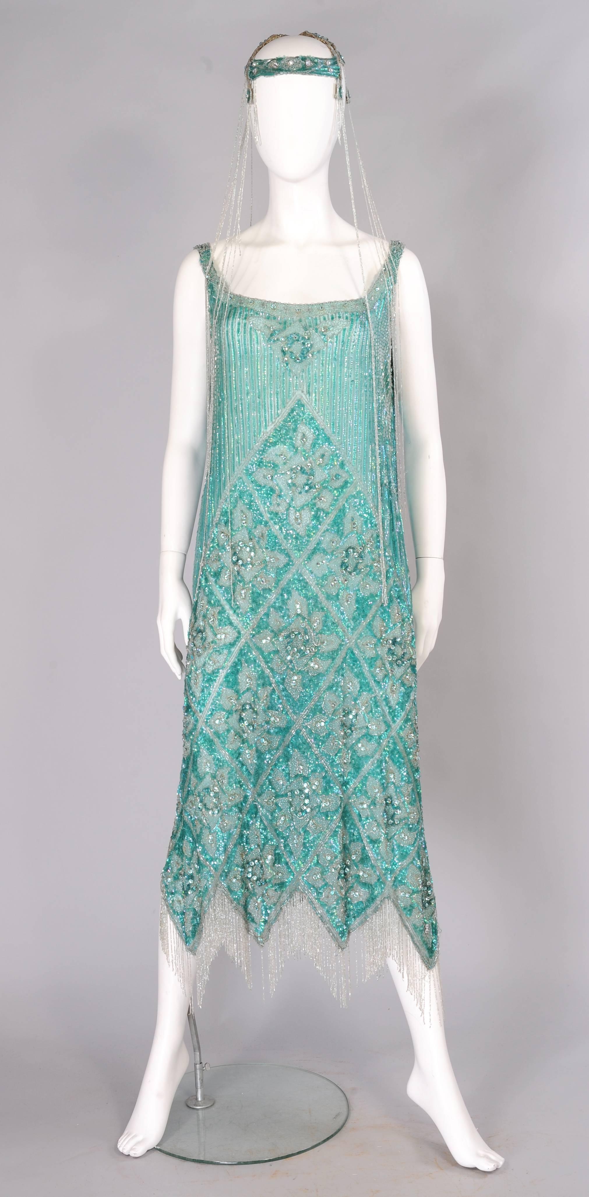 A beautiful shade of blue green silk is completely covered in beads. There are bugle beads, caviar beads and hundreds of sparkling rhinestones all set against rows and rows of opalescent green sequins. The dress has deep slits on each side and the