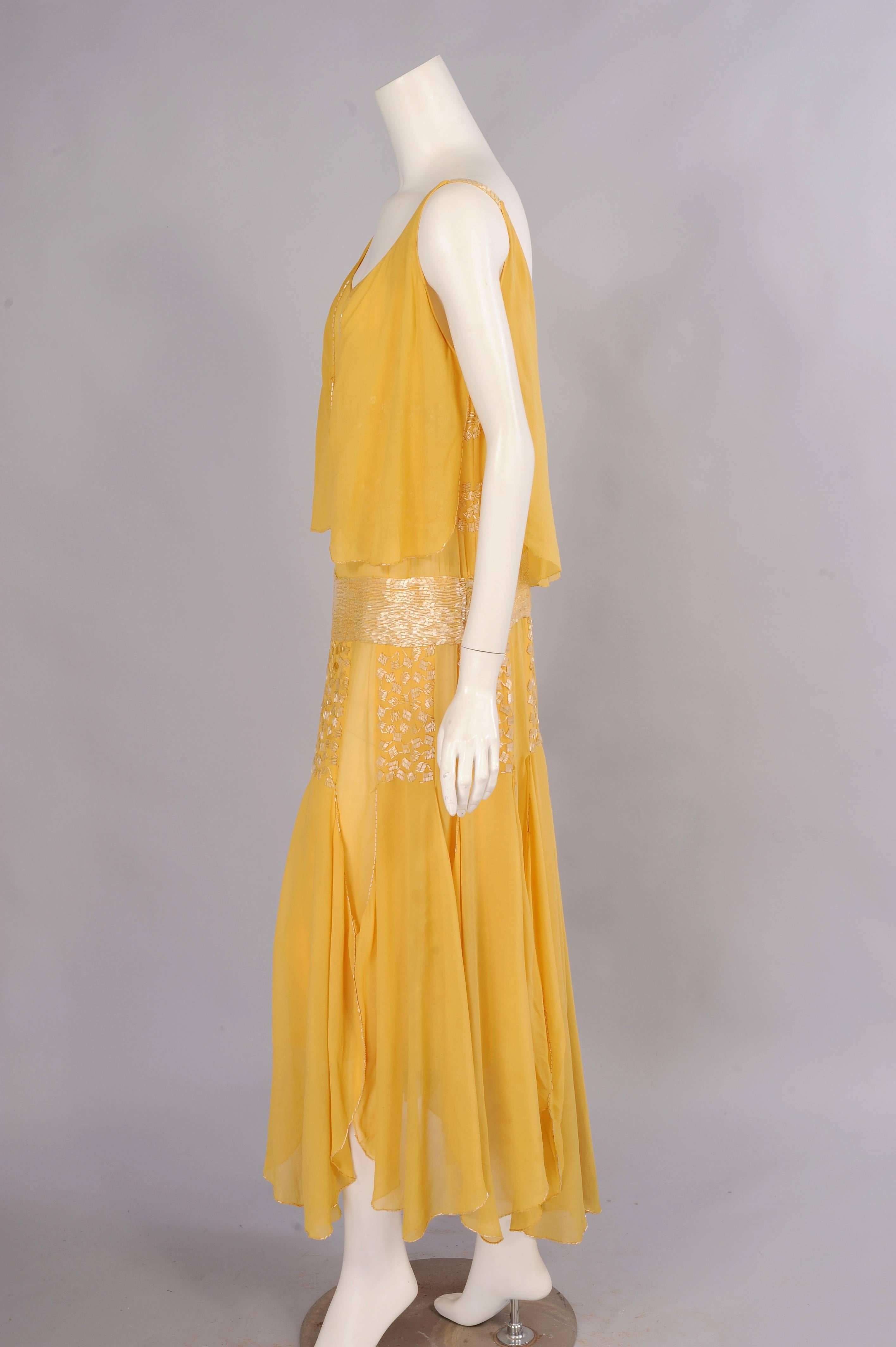 Dieses wunderschöne Kleid aus dem Hause Drecoll-Beer aus dem Jahr 1929 ist aus blassgelbem Seidenchiffon gefertigt:: der mit Perlen besetzt und drapiert ist.  Das Mieder ist mit diagonal verlaufenden Perlenreihen aus Perlenquadraten versehen. Eine