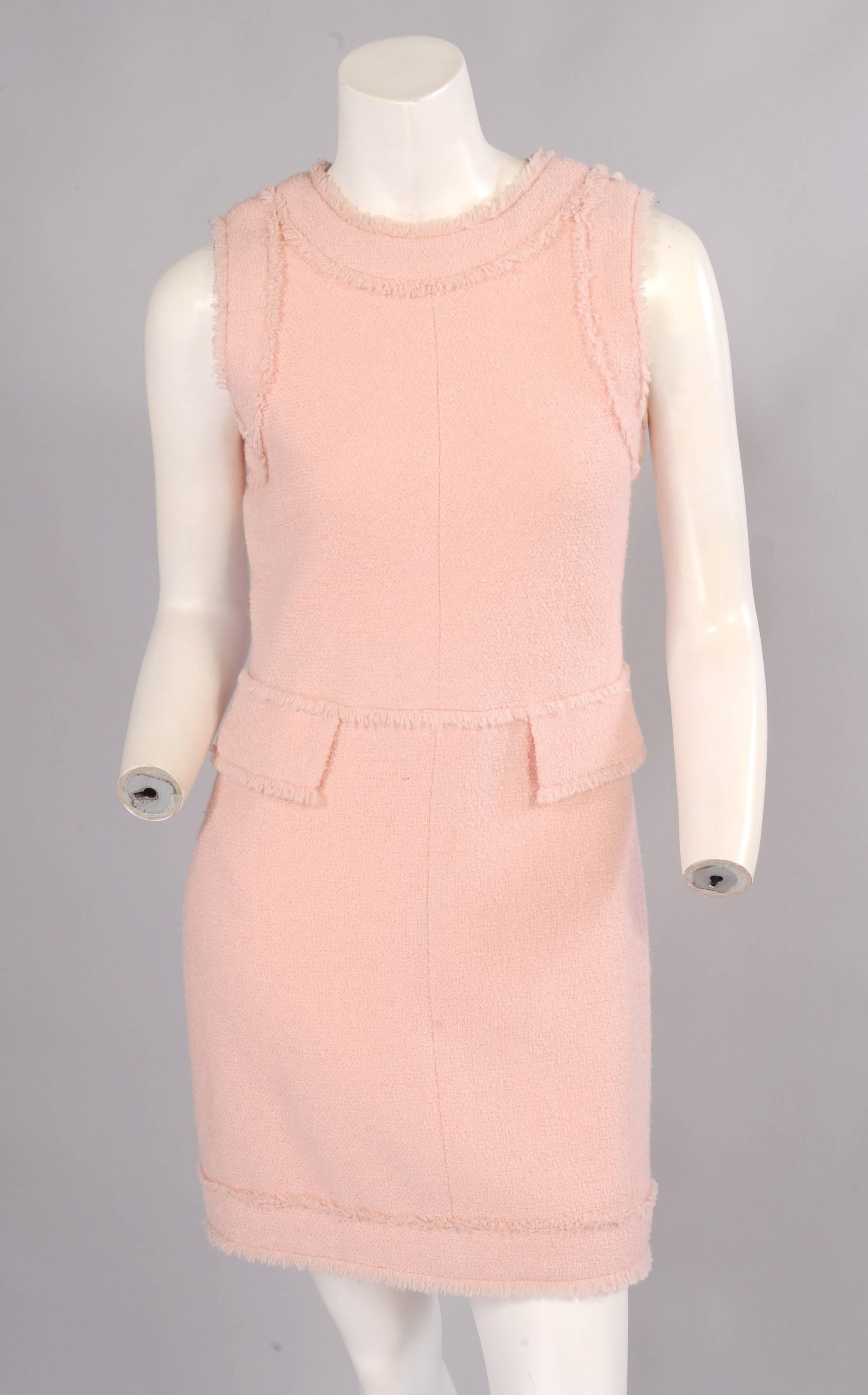Classic pale pink wool boucle is used for the sleeveless sheath and the lining of the patent leather coat. The dress has fringe trimmed bands and pockets. It buttons down the center back with concealed buttons and snaps. It is fully lined in pale