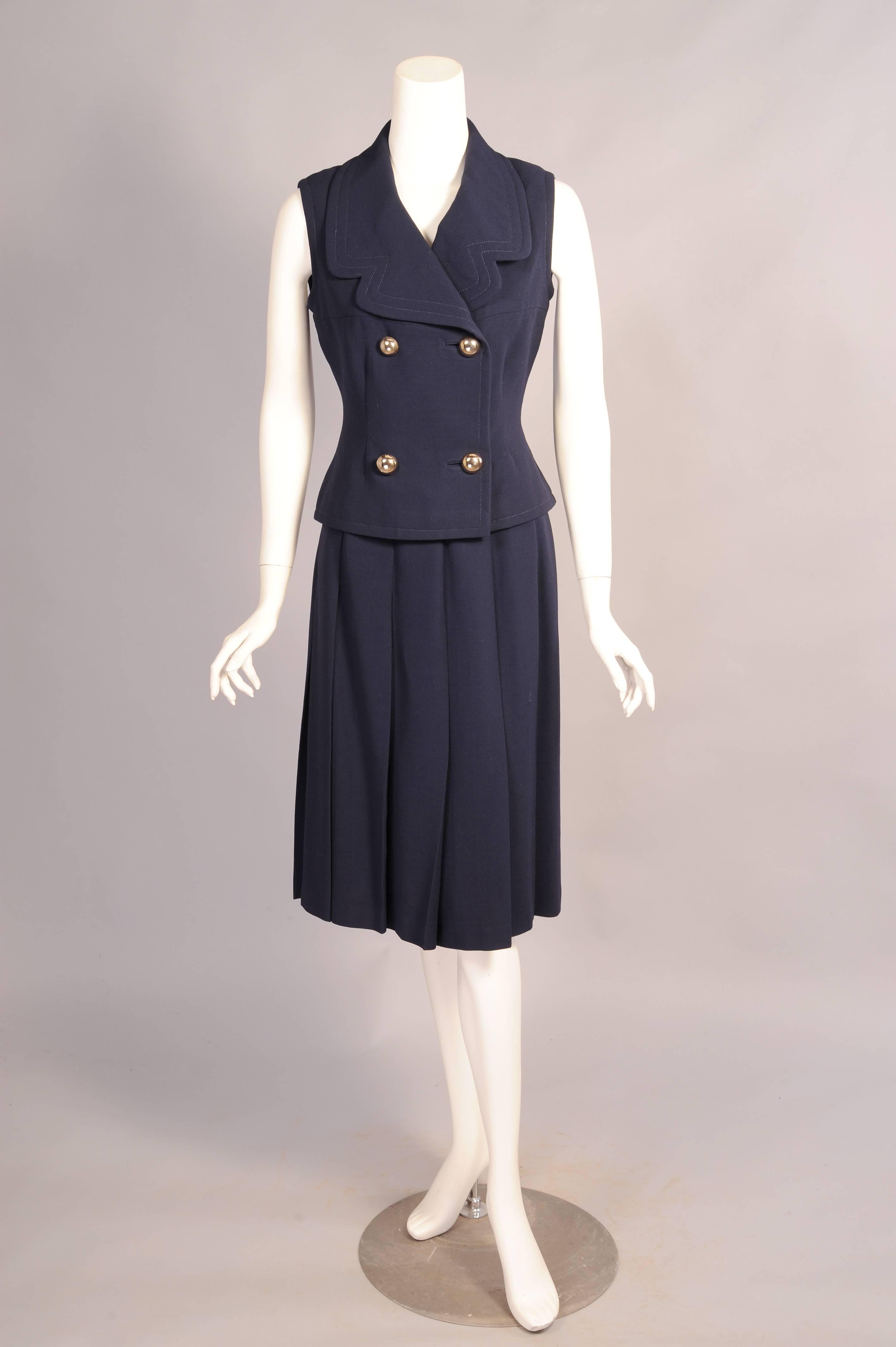 A modern take on a classic suit jacket, Cardin designed this one without sleeves. He added oversized notched lapels and four silver toned dome shaped buttons at the center front. The matching skirt has a wide flat waistband over the hips and