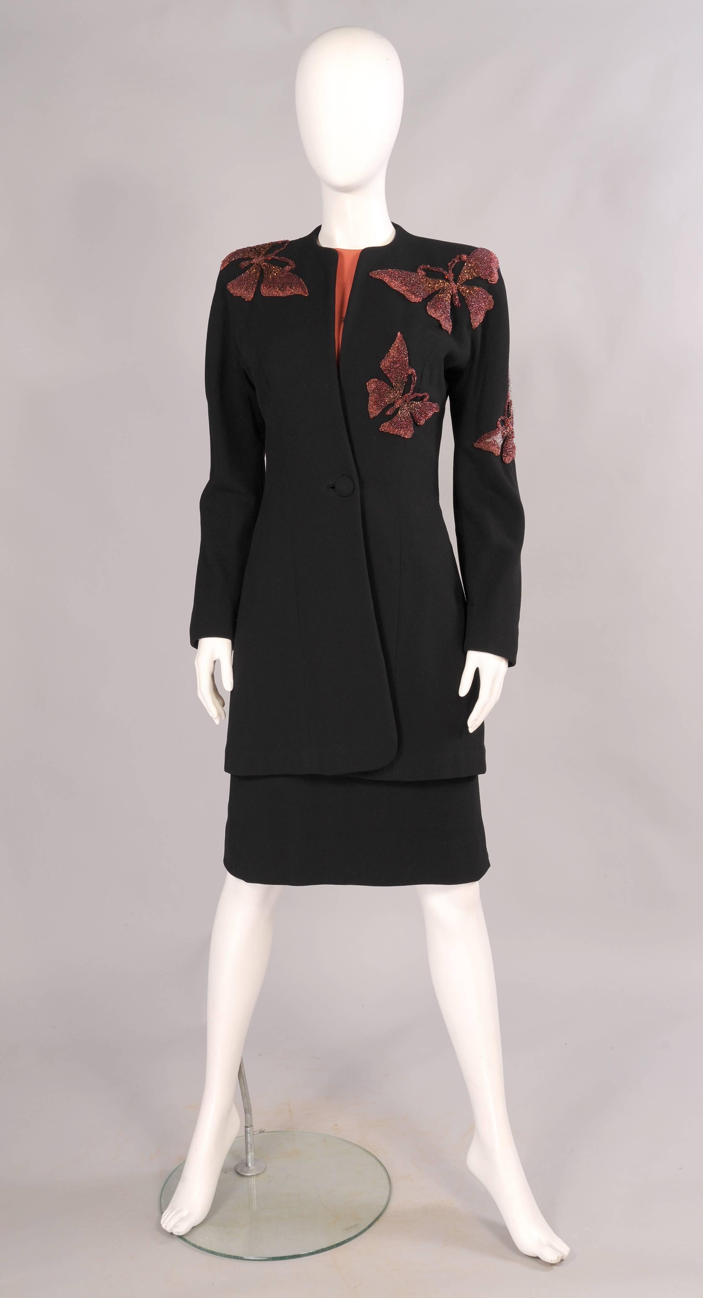 A fitted 3/4 length black wool coat is dramatically embellished with larger than life size beaded butterflies. The matching dress has a salmon colored bodice with a large butterfly on the left shoulder and a smaller one on the right hip of the black
