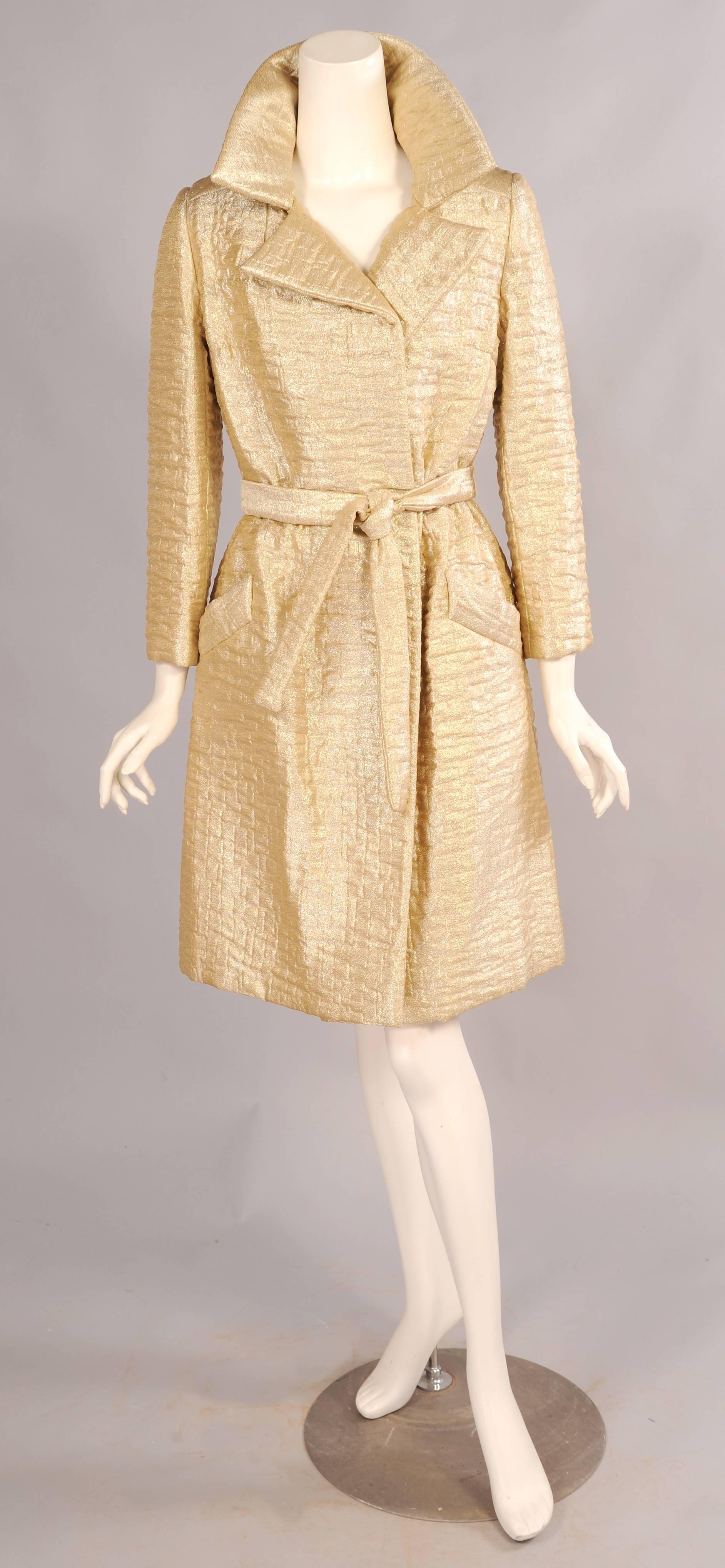 Timeless styling makes this great gold lame trench coat a perfect fit for any wardrobe. Retailed by Bonwit Teller in the 1960's the coat simply ties closed with a matching belt to accommodate a range of sizes. It is fully lined and in excellent