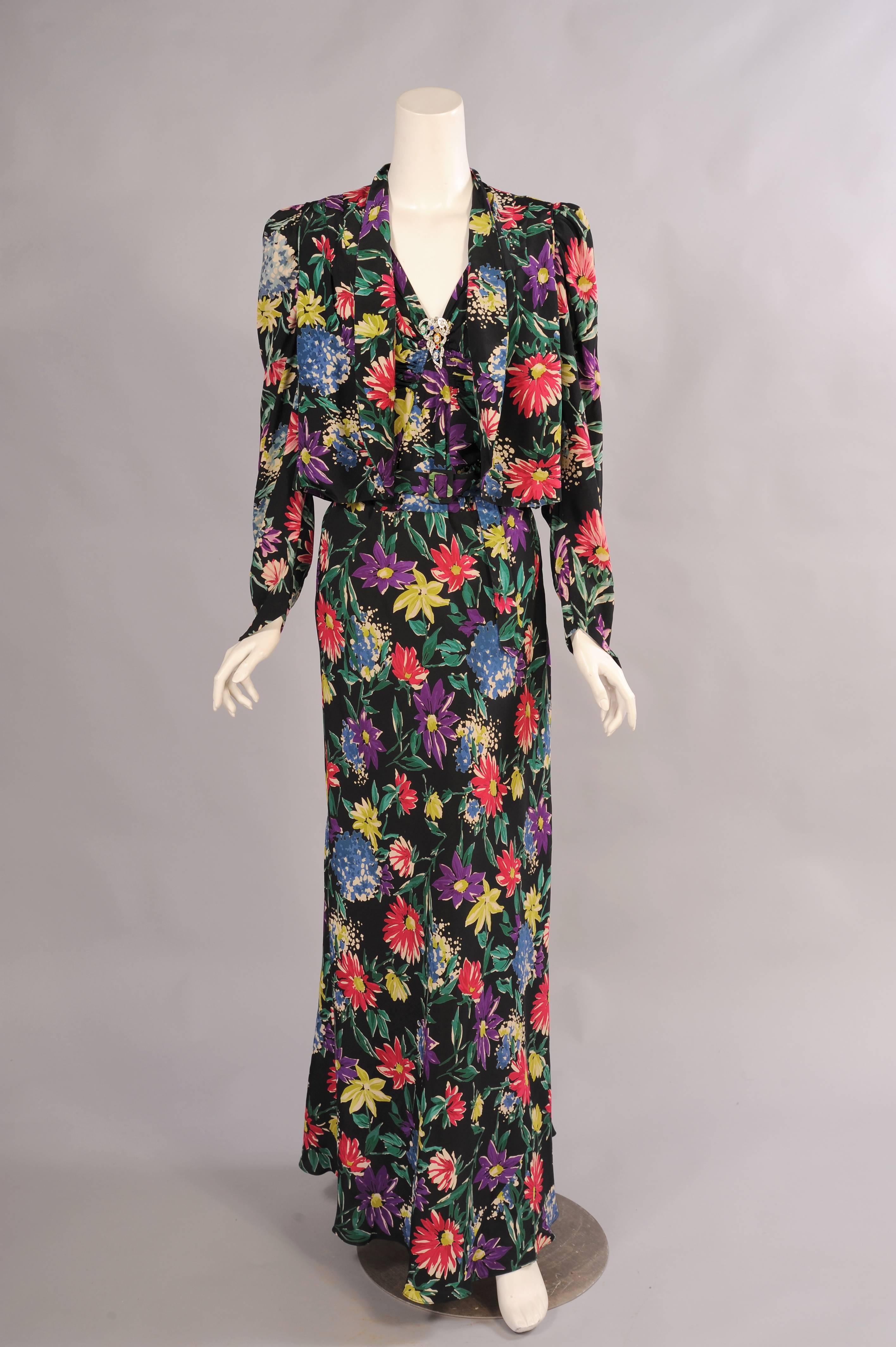 A gorgeous and colorful floral print is set against a classic black background for this late 1930's evening dress. With the addition of the jacket it can be worn in several ways. For a more covered up look the jacket can be pulled closed to create