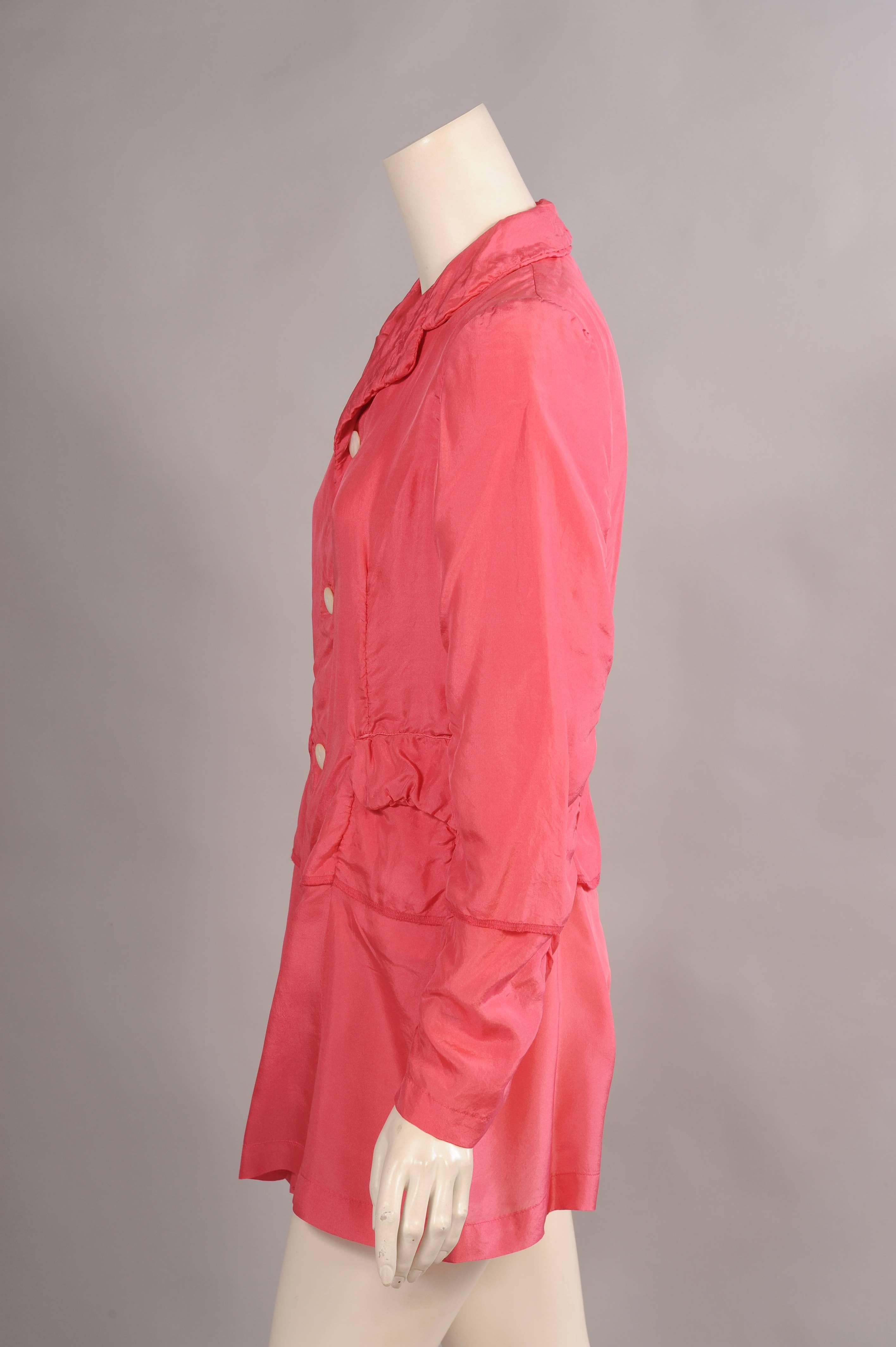 A modern take on the classic three button blazer, this piece from Comme des Garcons is made from two layers of pink silk. The jacket has a notched collar, three buttons and two flap pockets. The seams are lightly gathered and the lining extends
