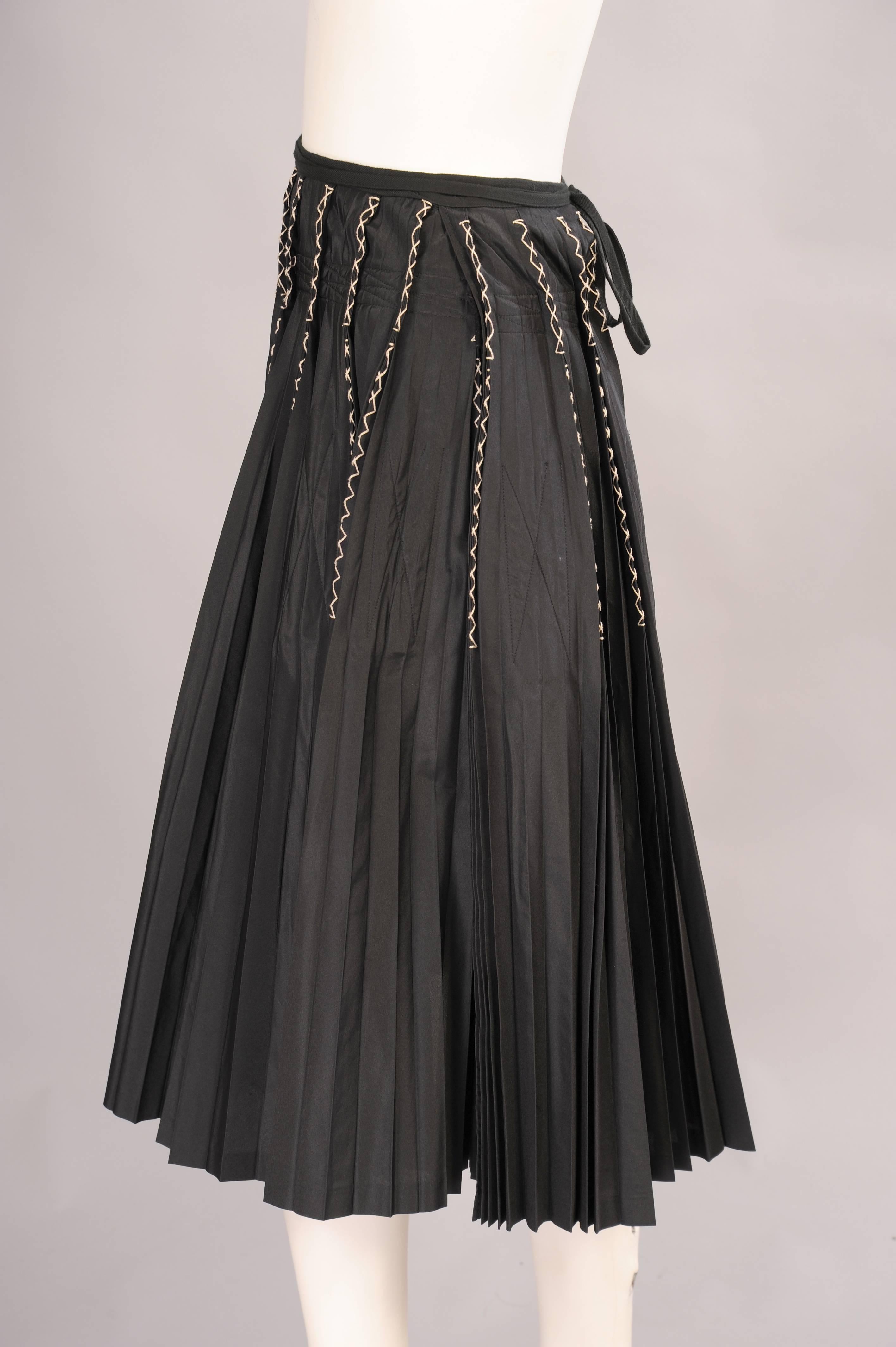 White embroidery is used to stitch some of the pleats together on this great silk blend wrap skirt from Yohji Yamamoto. An interior band around the hips  and rectangles in the skirt insure the pleats will stay pleated. A black tape is used for the