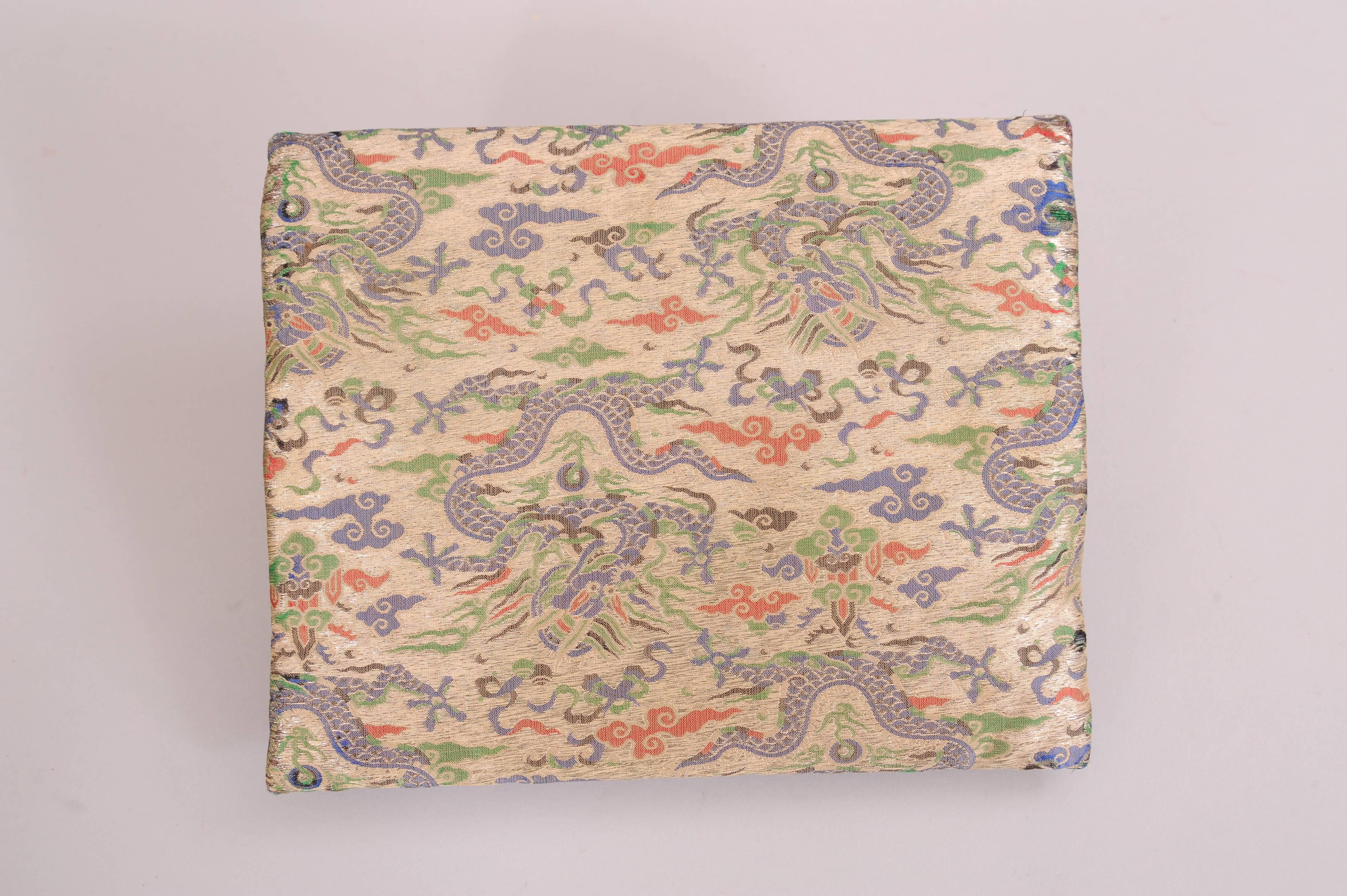 This fold over clutch in a metallic woven fabric has Asian inspired dragons and clouds in red, blue and green. There is an interior hinged frame, a satin lining and one slip pocket. The bag comes from the J.P. Morgan family by way of a museum de