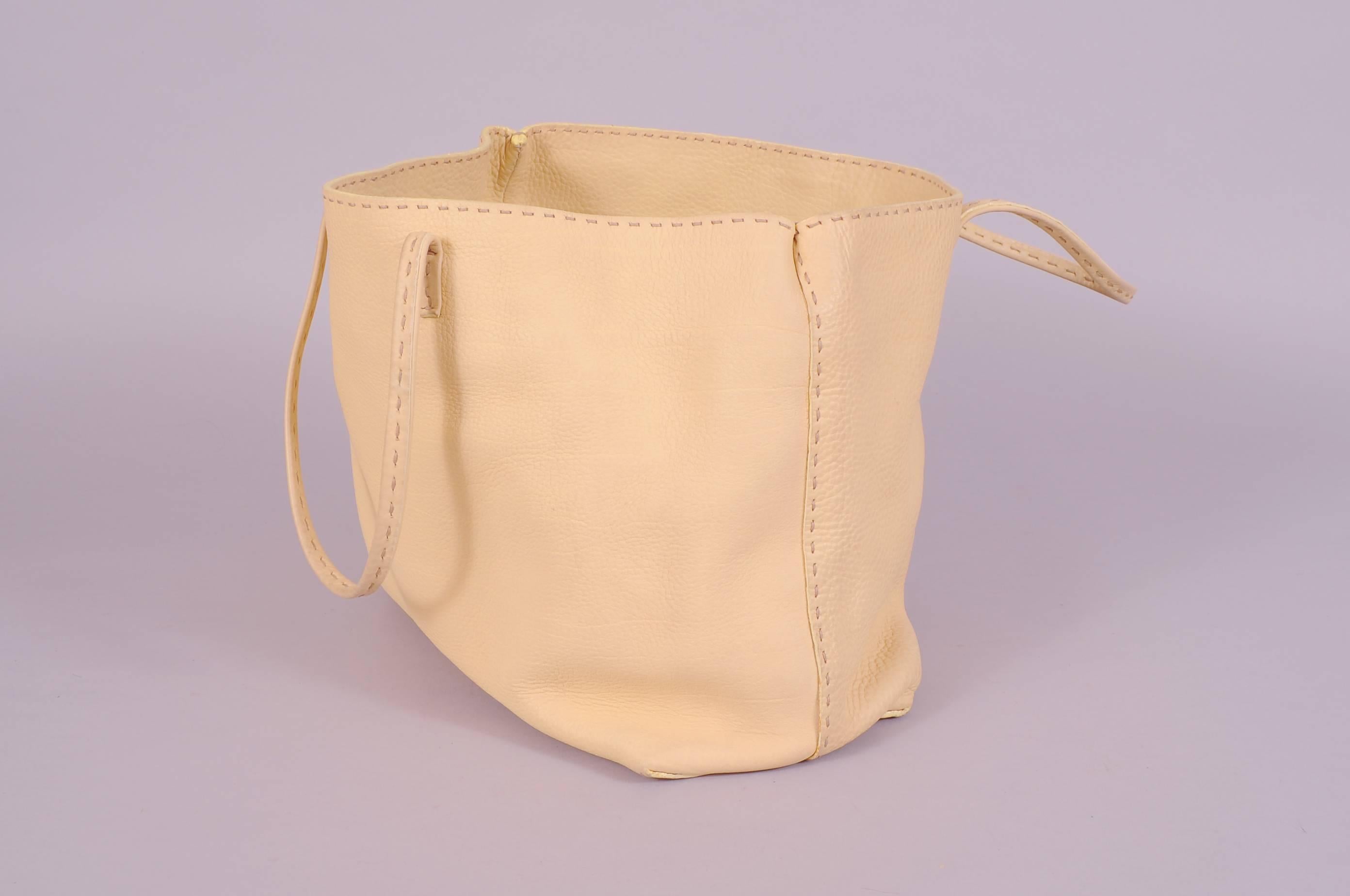 Pale butter yellow leather is used for this hand made tote. The straps and seams are finished with hand stitching in a natural color thread. The interior of the bag is a slightly darker yellow suede and there is one slip pocket and a metal plaque