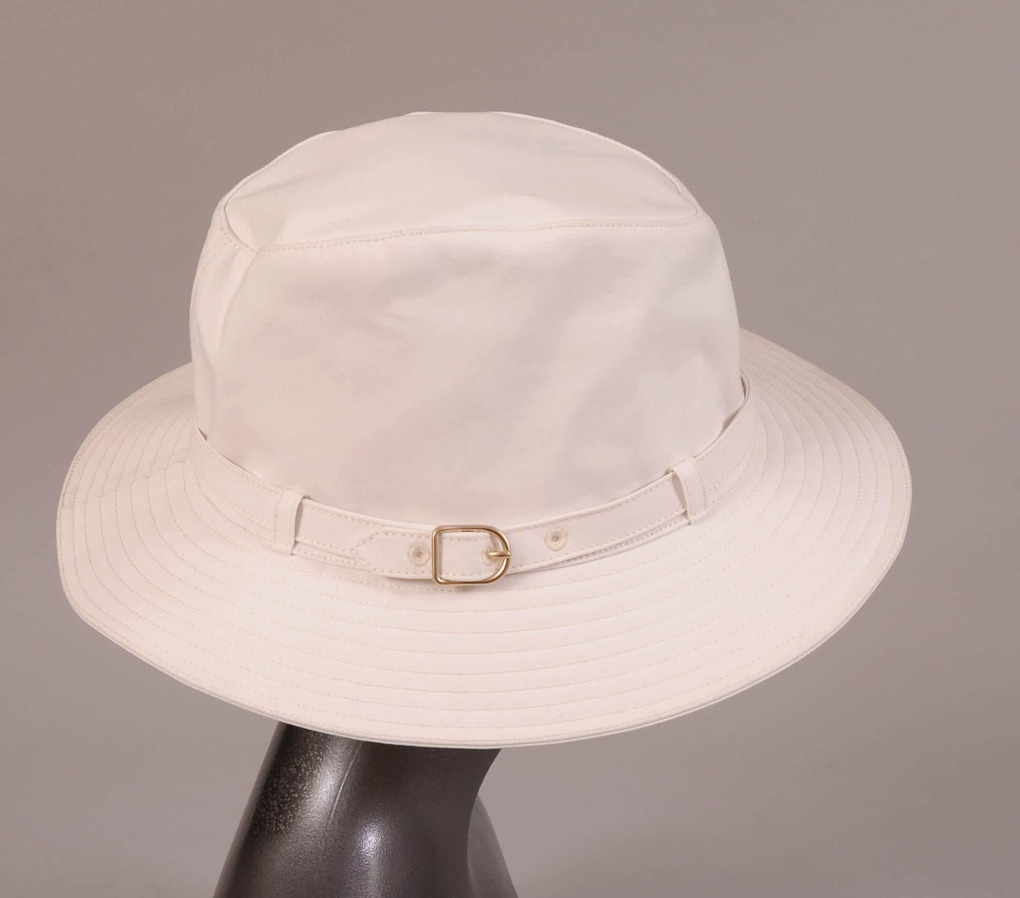 A play on the classic fedora, this waterproof hat has a high crown, decorative hat band with metal buckle and a channel quilted brim. It is lined in white linen and still bears the Hermes hang tag. It is in excellent, unworn condition and is marked