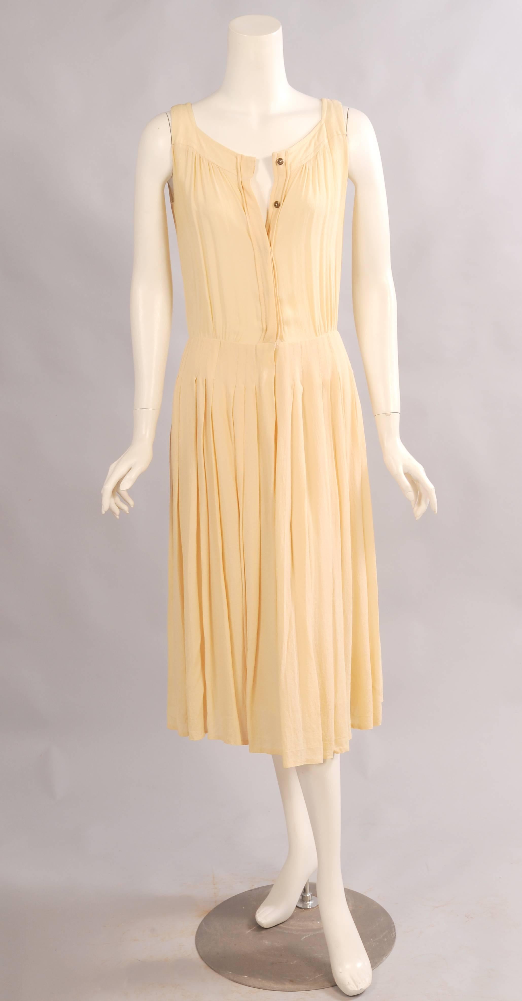A perfect little summer dress this butter yellow silk crepe dress has front and back yokes over a gently gathered bodice. The dress buttons at the center front with concealed meatl buttons. The silk lined skirt has stitched down pleats over the hips