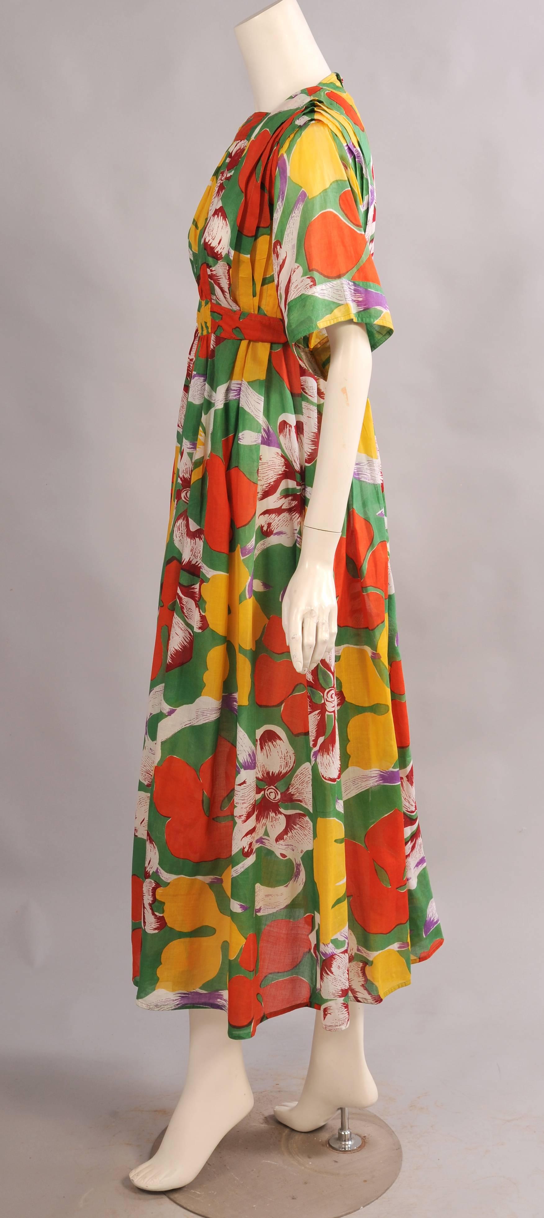 Colorful large scale tropical flowers on a bright green cotton background make this a great summer dress designed by Jean Muir in the 1970's. The dress has a square neckline, vertical pleats on the bodice, two [pockets and an attached belt. It