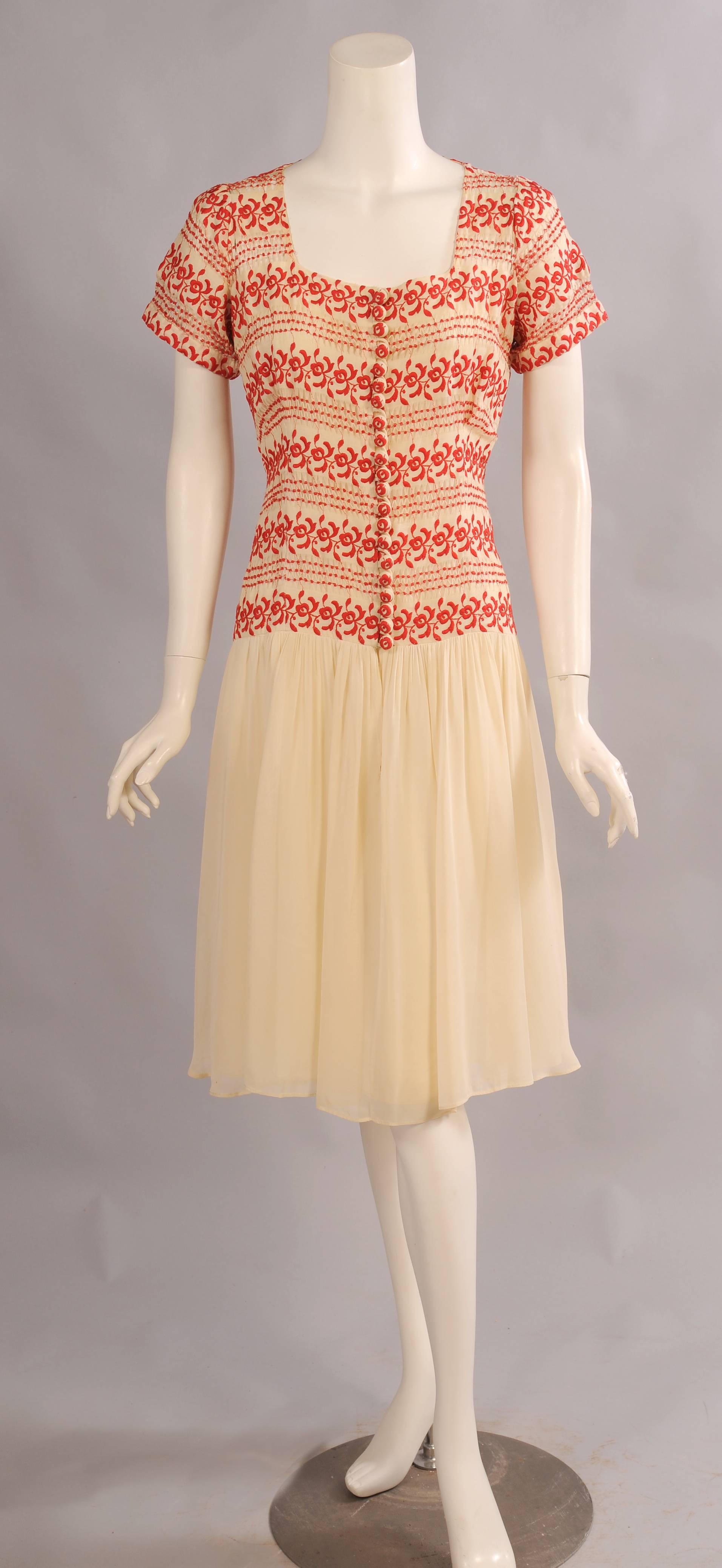 Drawn work and embroidery in red on cream linen are used for the bodice of this 1930's dress with a dropped waistline. The bodice is lined from the bust line to the hips and closes at the center front with 21 embroidered buttons and loops. The