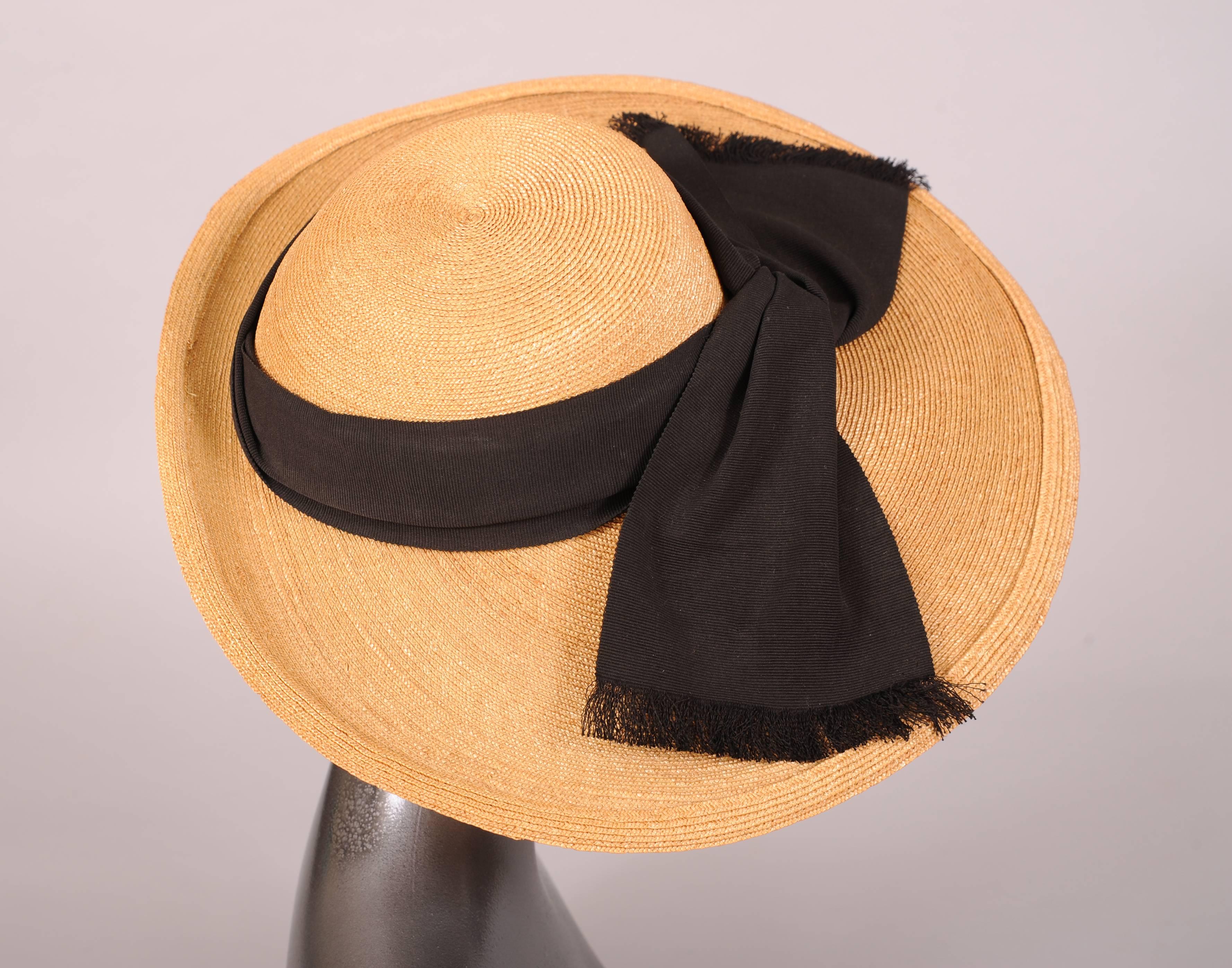 A sweet summer hat in natural straw with a wide brim in front, this hat is decorated with a wide black gros grain ribbon wrapping the crown. A casual knot is at the center front and the ribbon has fringed edges. It is in excellent condition and was