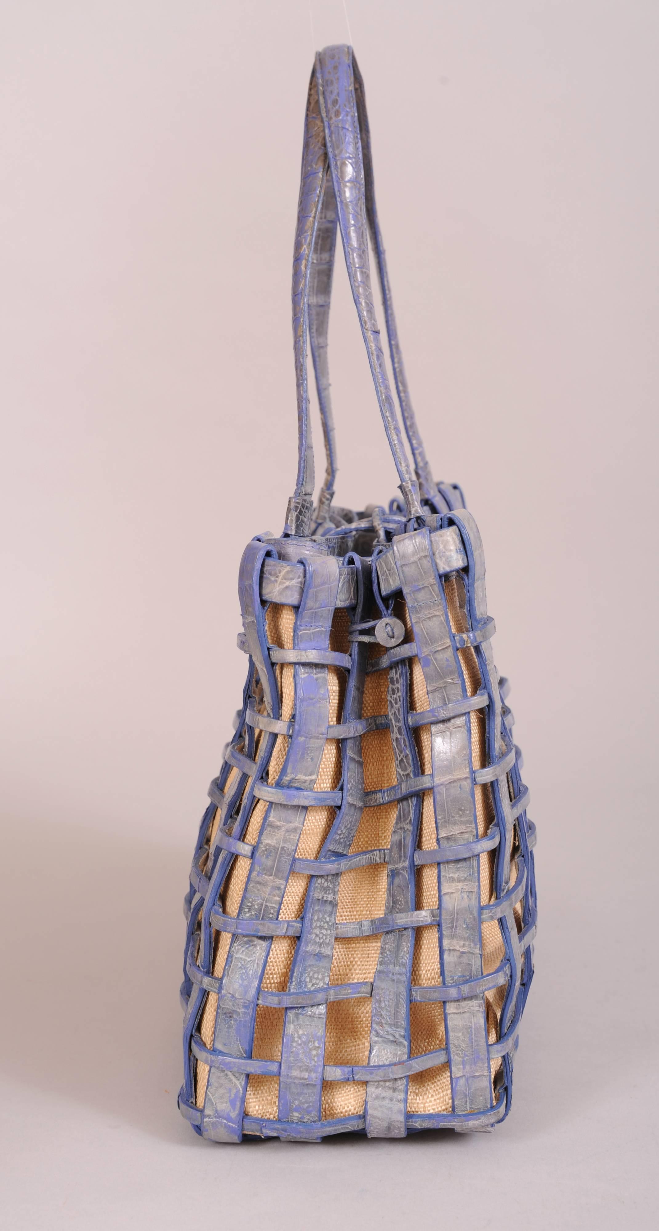 A woven blue crocodile cage bag matches the blue crocodile top edge of the removable woven raffia straw bag insert. This bag is lined in pale blue suede. it has a center zipped compartment and two open sections. One of these has a zippered pocket