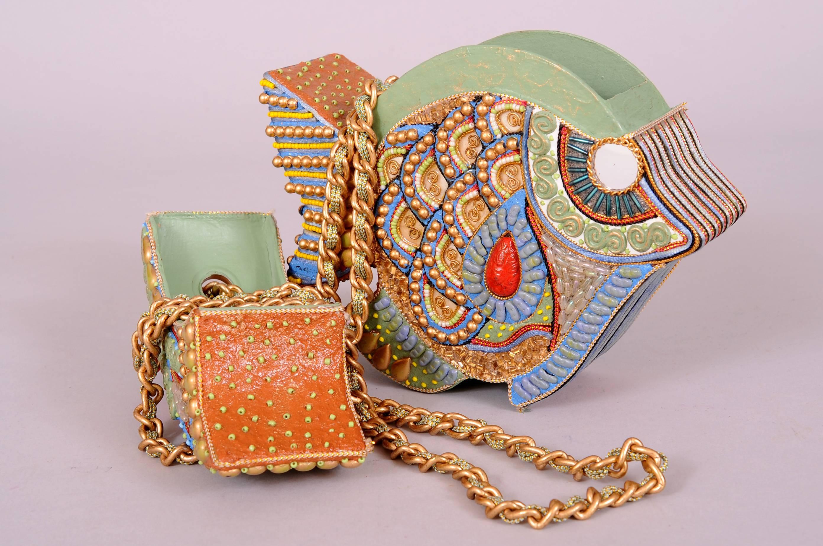 This wooden fish shaped shoulder bag is just amazing. Every inch of the surface is covered with embellishments, including beads, paint and mirror. The top of the bag lifts up for easy access. The metal link strap is threaded with a green and gold