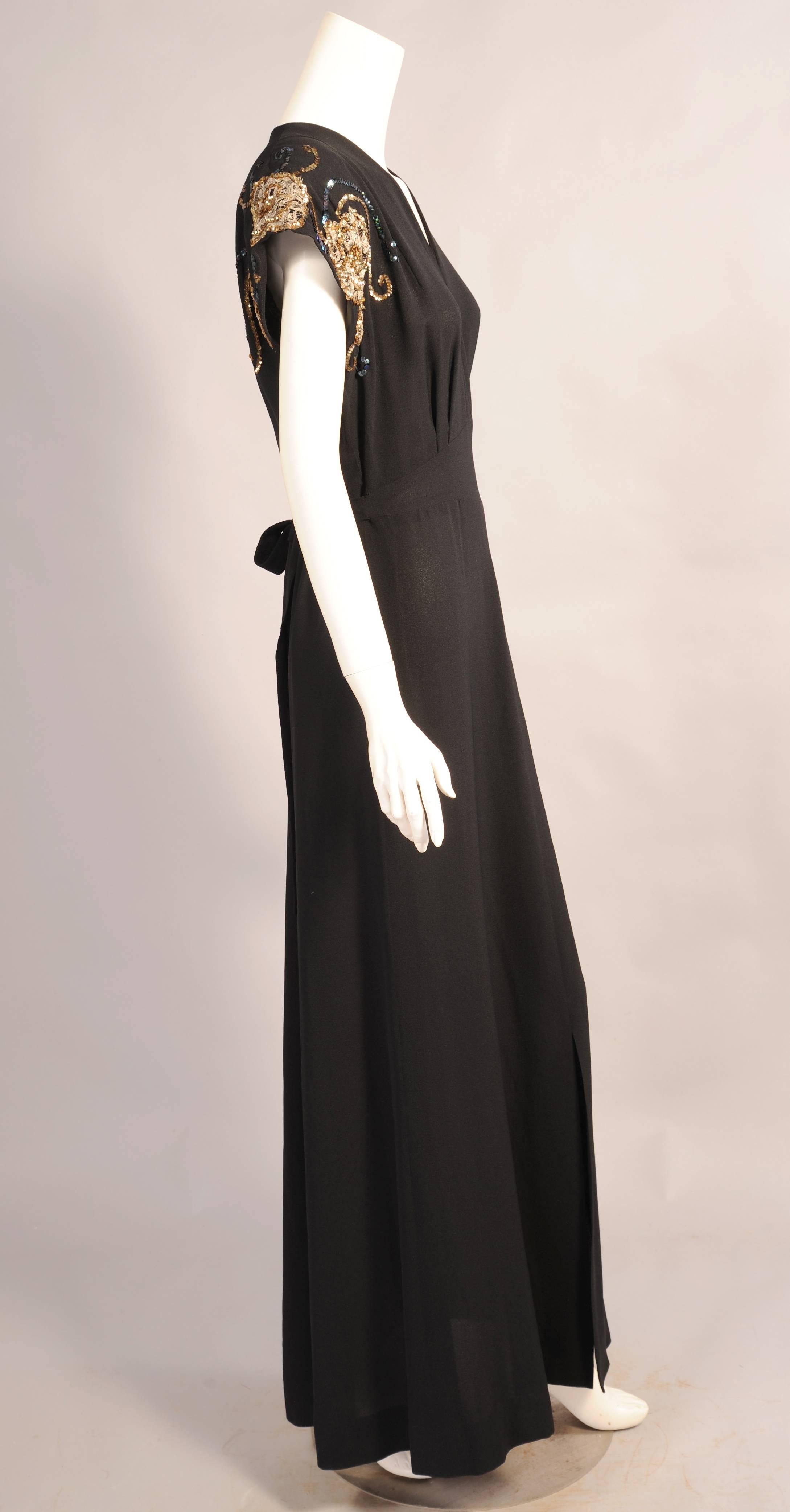 Elegant and easy to wear this black crepe dress from the late 1930's or very early 1940's  has a V shaped neckline and cap sleeves with metallic lace and sequin trim. The front of the dress has an attached cummerbund that ties in back. There is a