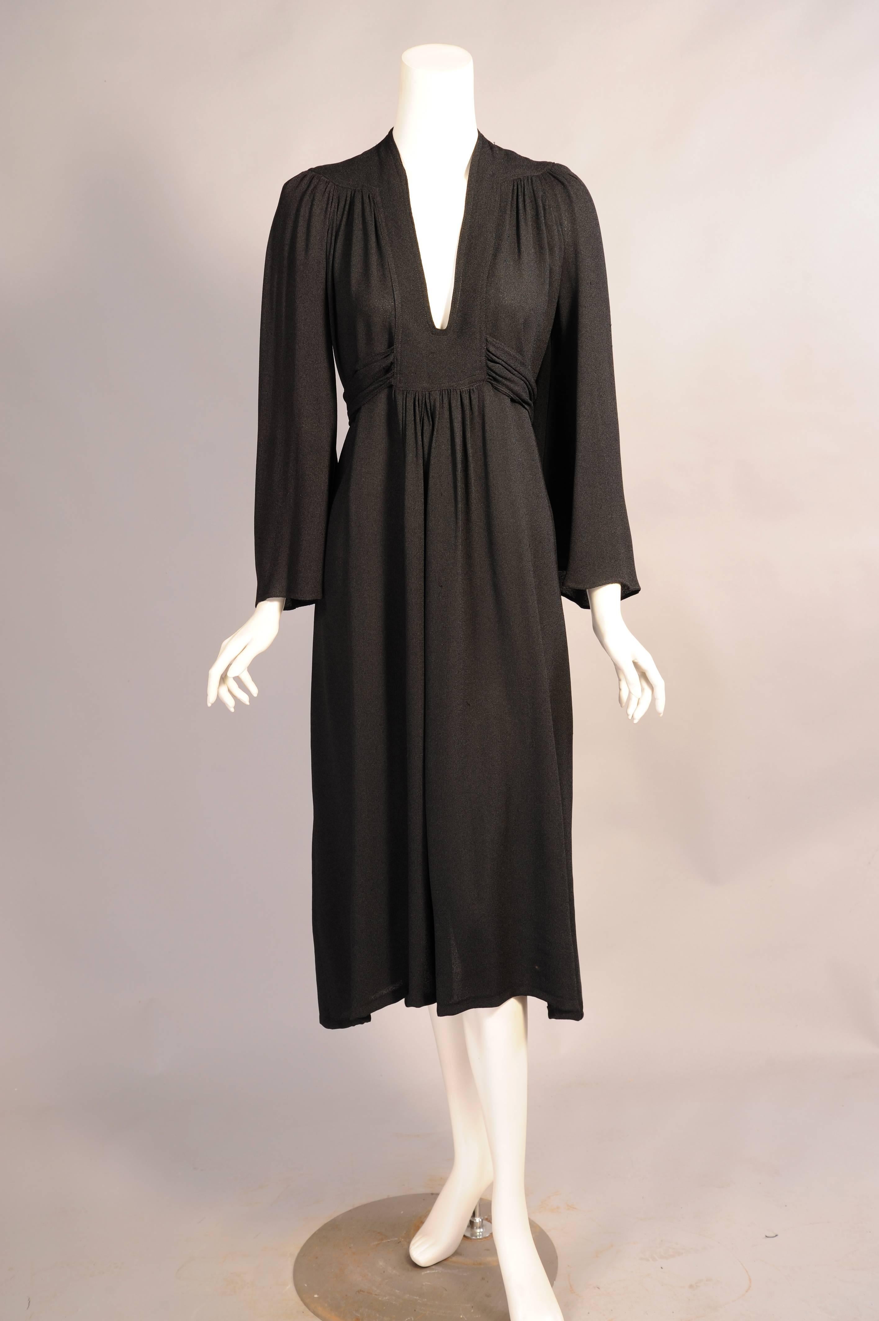A [plunging neckline and a tie under the bust turn this black crepe dress into a sexy little black dress.  The dress has a front and back yoke and the gathers flow from this point. The sleeves are long and full. The dress is in excellent condition