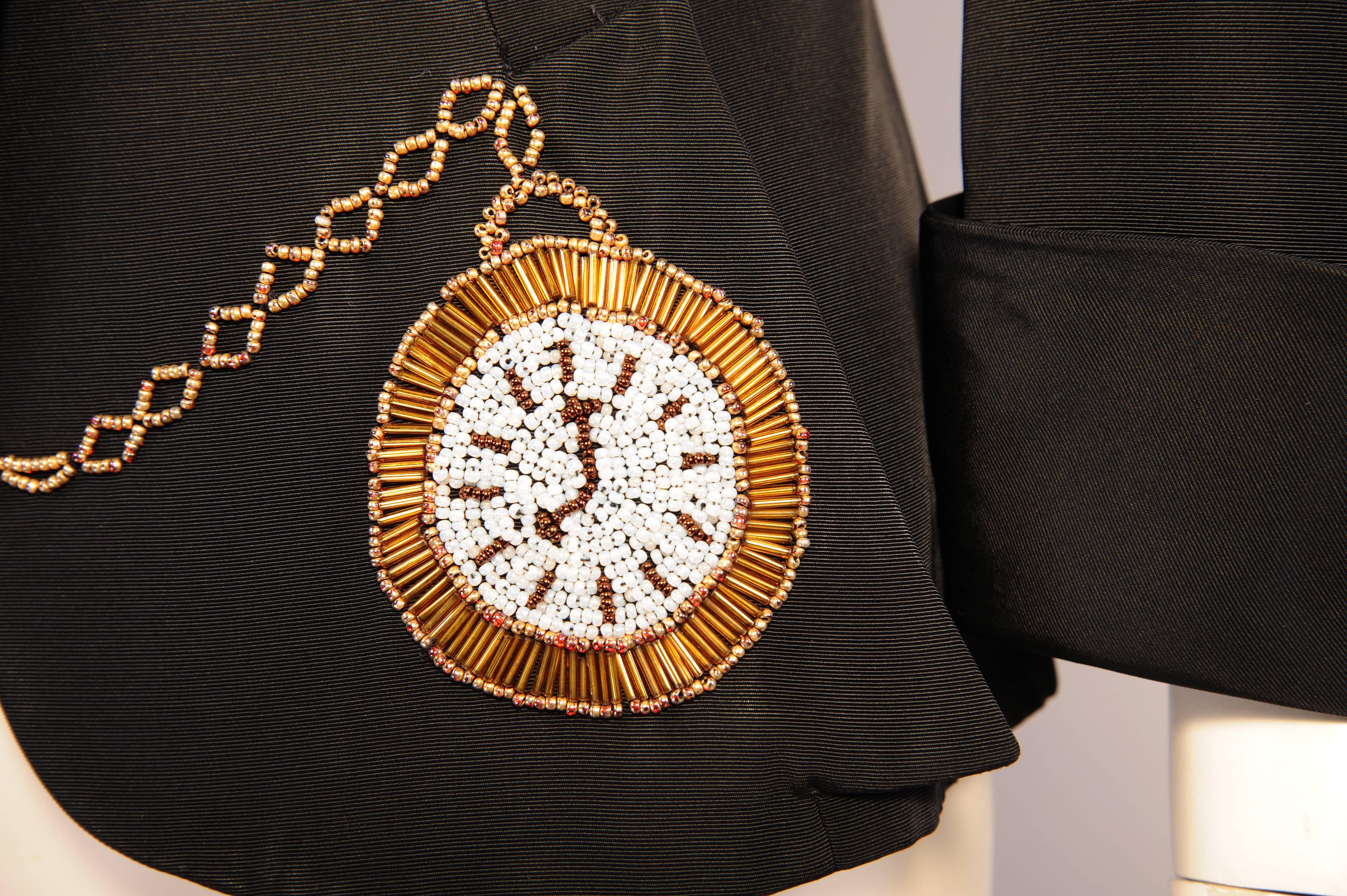 In the style of Elsa Schiaparelli this jacket has a whimsical beaded pocket watch theme. The classic notched lapel has a beaded watch face on the right lapel with a beaded chain and diamante fob circling around the neck to the top of the left lapel.