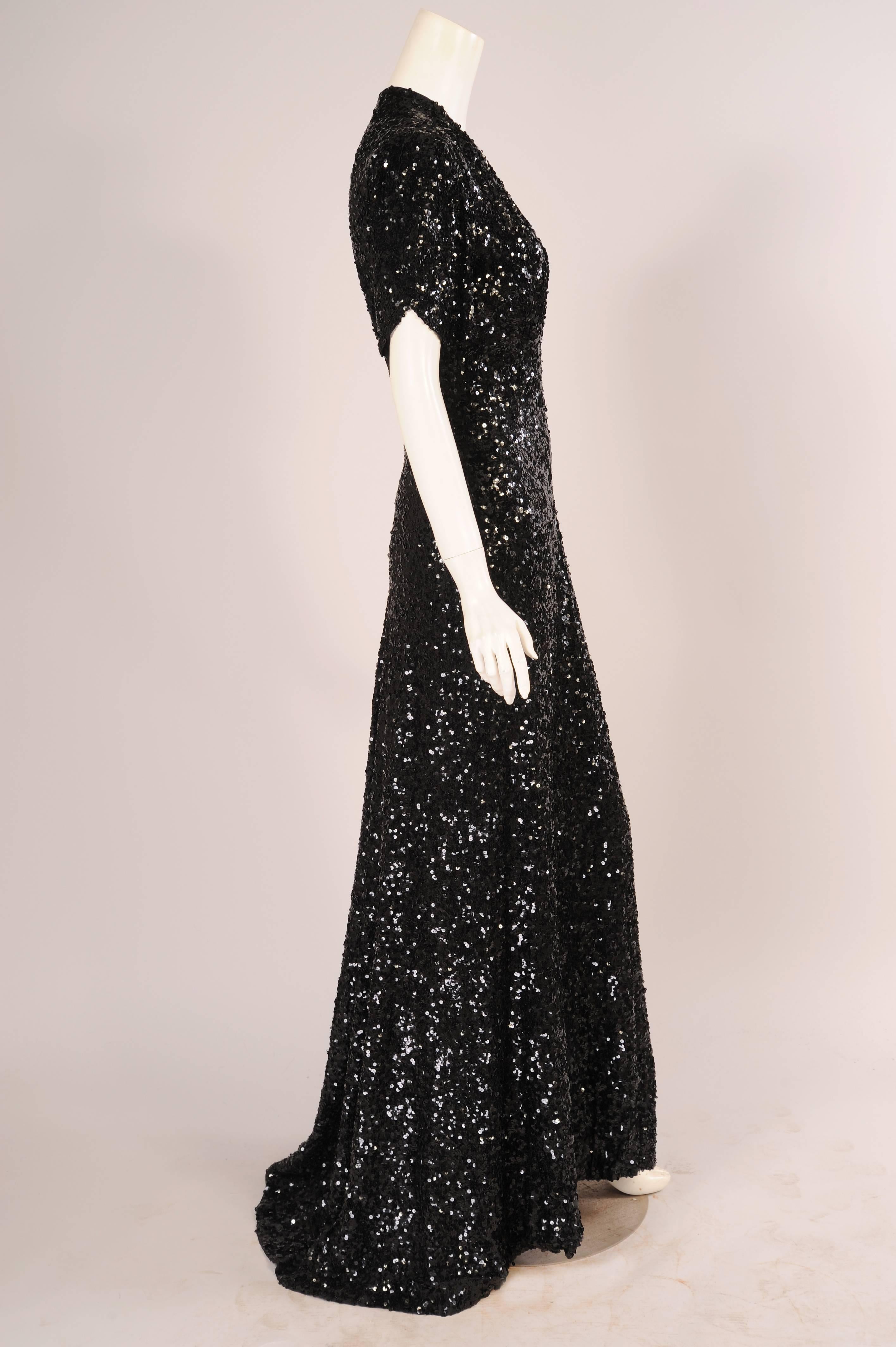 This dress is so evocative of the elegance and glamour of 1930's clothing. The black silk dress is lavishly beaded with glistening black sequins covering every bit of the dress. It has a deep plunging neckline, short sleeves with a curved detail, a