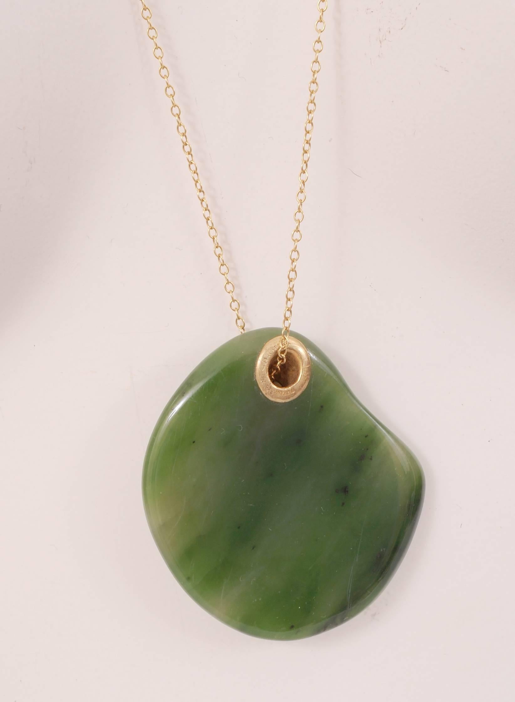 A lovely large piece of green jade has an 18 karat  gold diagonal opening threaded with an 18 karat gold chain. It is signed on the back opening and the chain and it is in excellent condition. It comes with a Tiffany suede pouch and