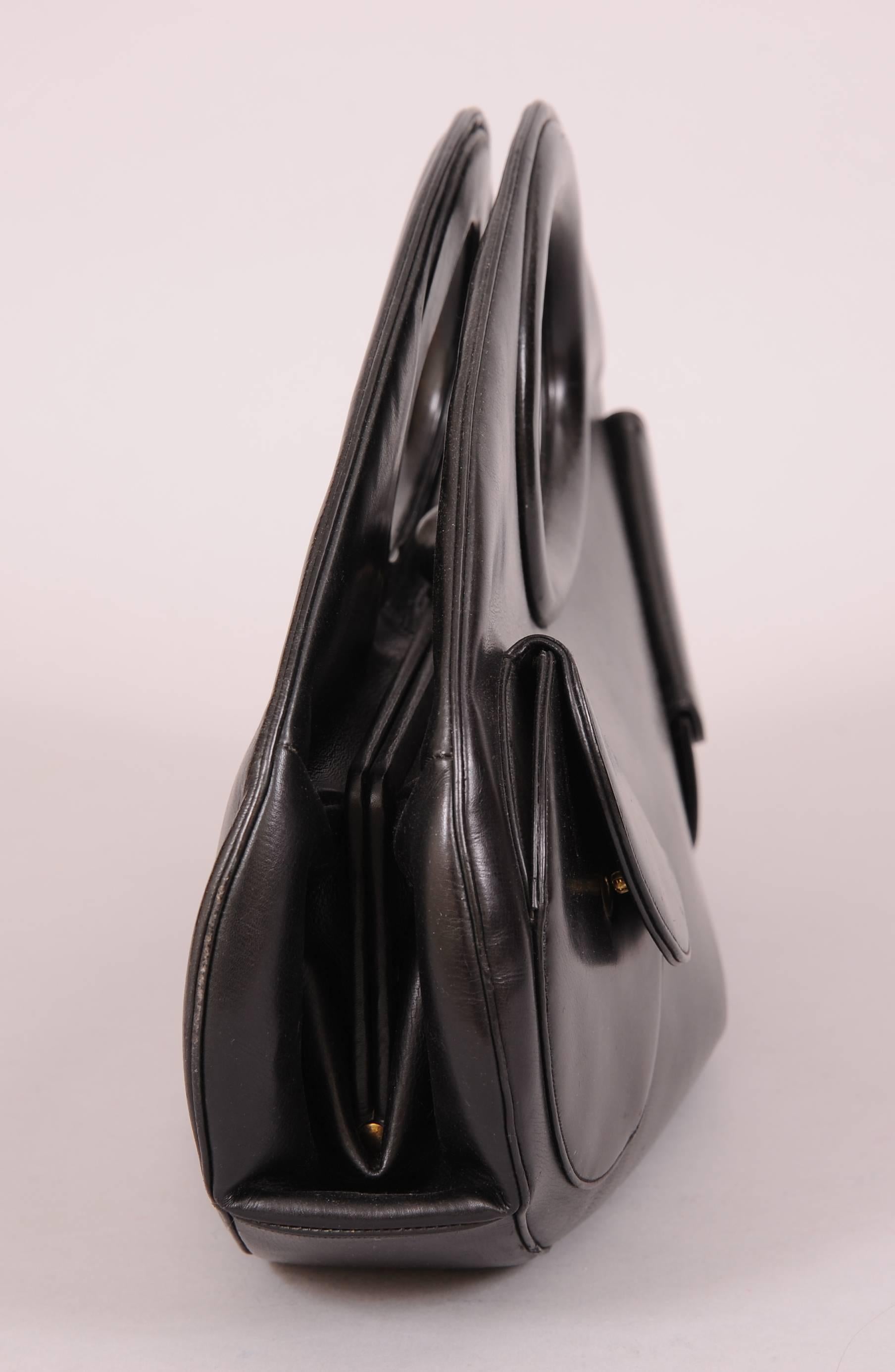 What a great shape! This bag is a large modified oval, with the handle opening inside the oval. There are two leather pockets with snap closure on the front of the bag. A black leather ball closure sits in the middle of the bag. The interior is