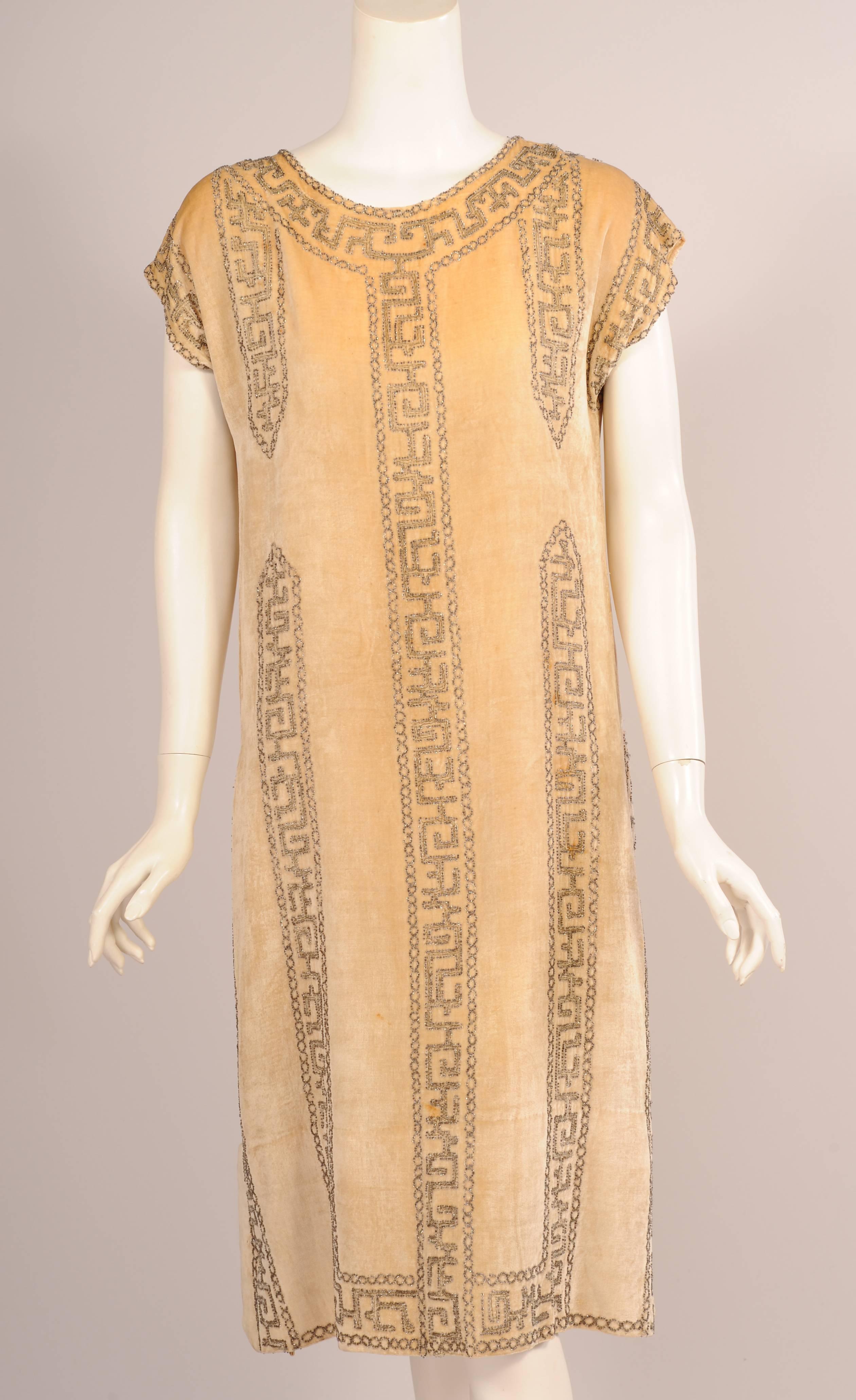 This elegant cream colored velvet flapper dress is embroidered with metallic thread and beaded in an Asian inspired design. The dress has a round neckline, cap sleeves and deep slits om either side. It was Made in France and is labeled a Rue de la