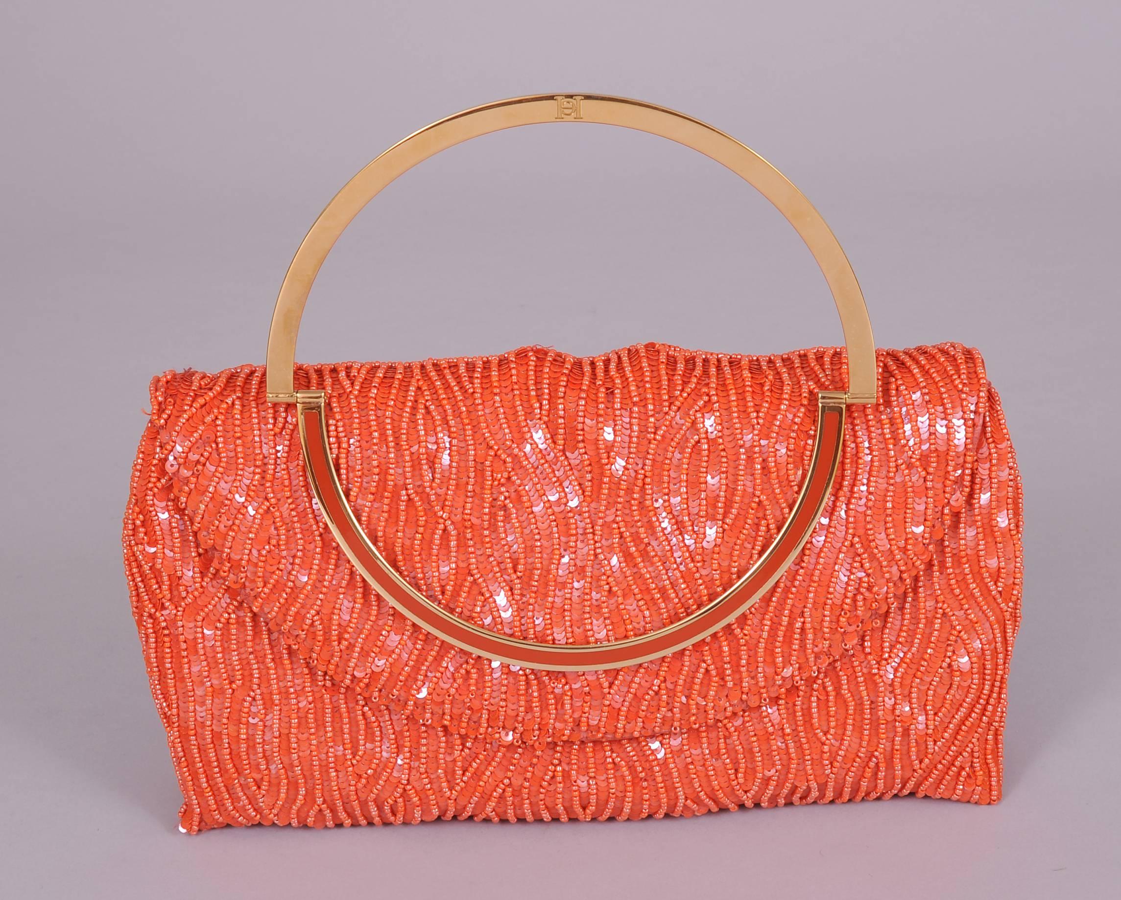 A witty coral bag is beaded in an undulating pattern of bugle beads to suggest coral branches. This is set against a background of coral sequins. The bag has a folding gold toned handle with a matching fixed gold and coral band. The interior is