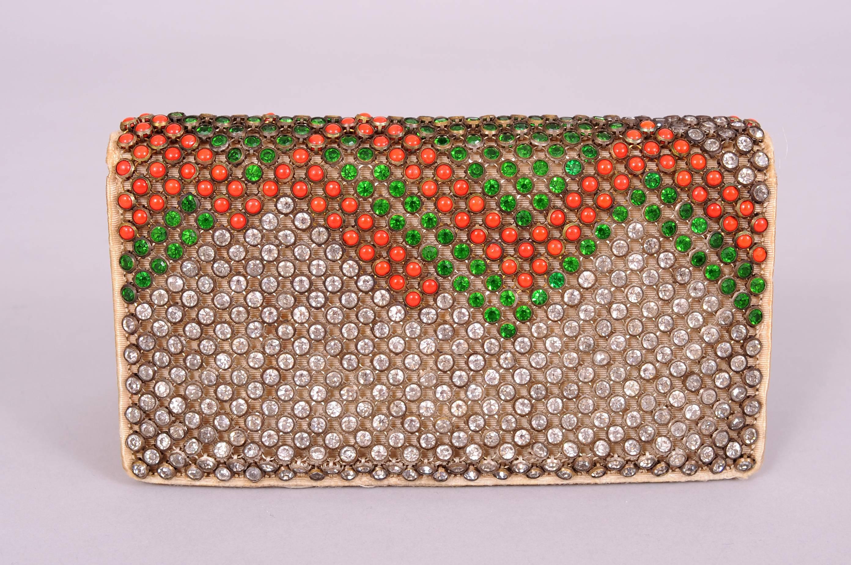 This fabulous little bag is completely covered with bezel set clear crystal, green crystal and cabochon coral stones in an Art Deco design. There are no missing stones. The interior is cream silk moire with a mirror in the top and two slip pockets.