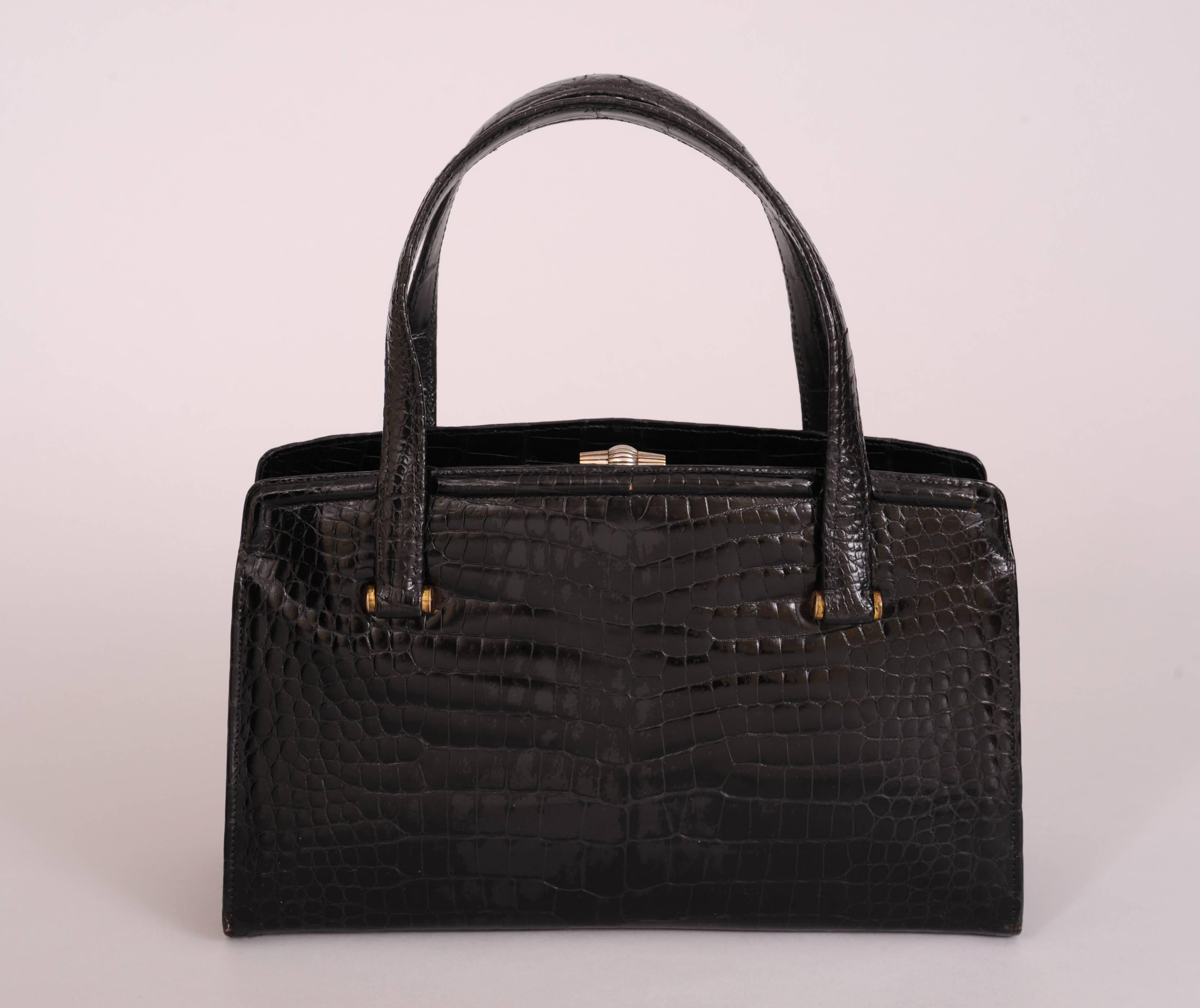 A chic black crocodile bag from Gucci has a leather lined center section with a silver clasp. There is a zip pocket and four slip pockets inside. There is a generous leather lined open pocket on each side of the center. The bag is in excellent