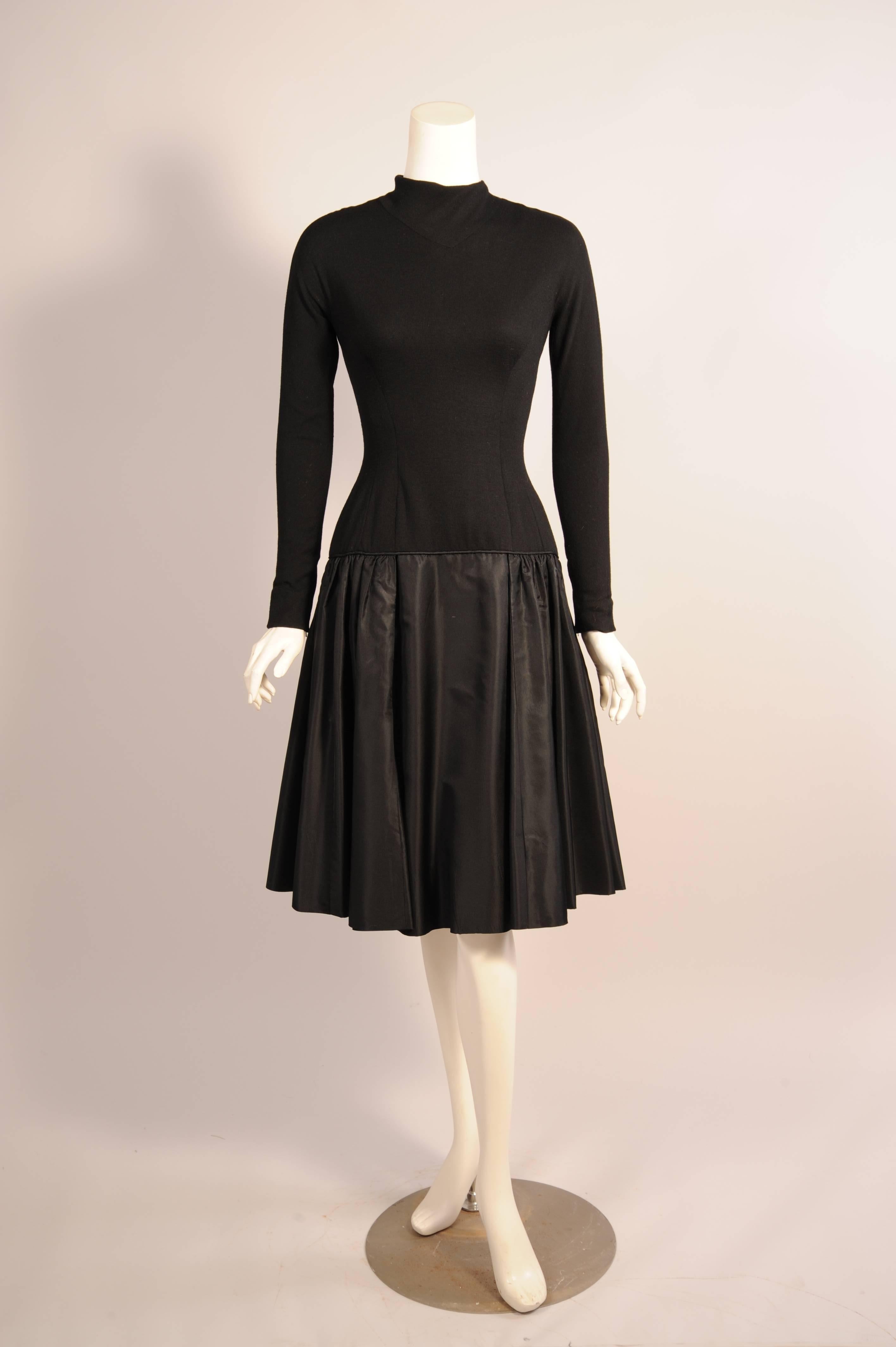 This chic little black dress comes from the estate of a lady who wore couture. Sadly there is no label in this piece. The anonymous designer used black wool jersey for the elongated bodice. It has a mock turtleneck, long sleeves with little zippers