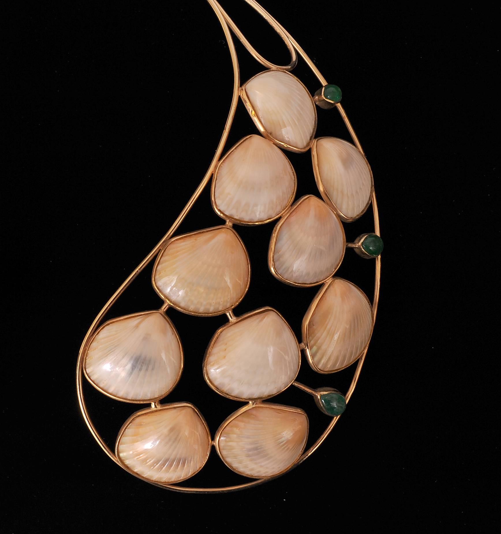 This striking piece of jewelry is a true work of art designed by Marguerite Stix in 1970. The collar shaped necklace has ten shells on each side edged with gold. Three cabochon emeralds add color to each side and the whole shell element is