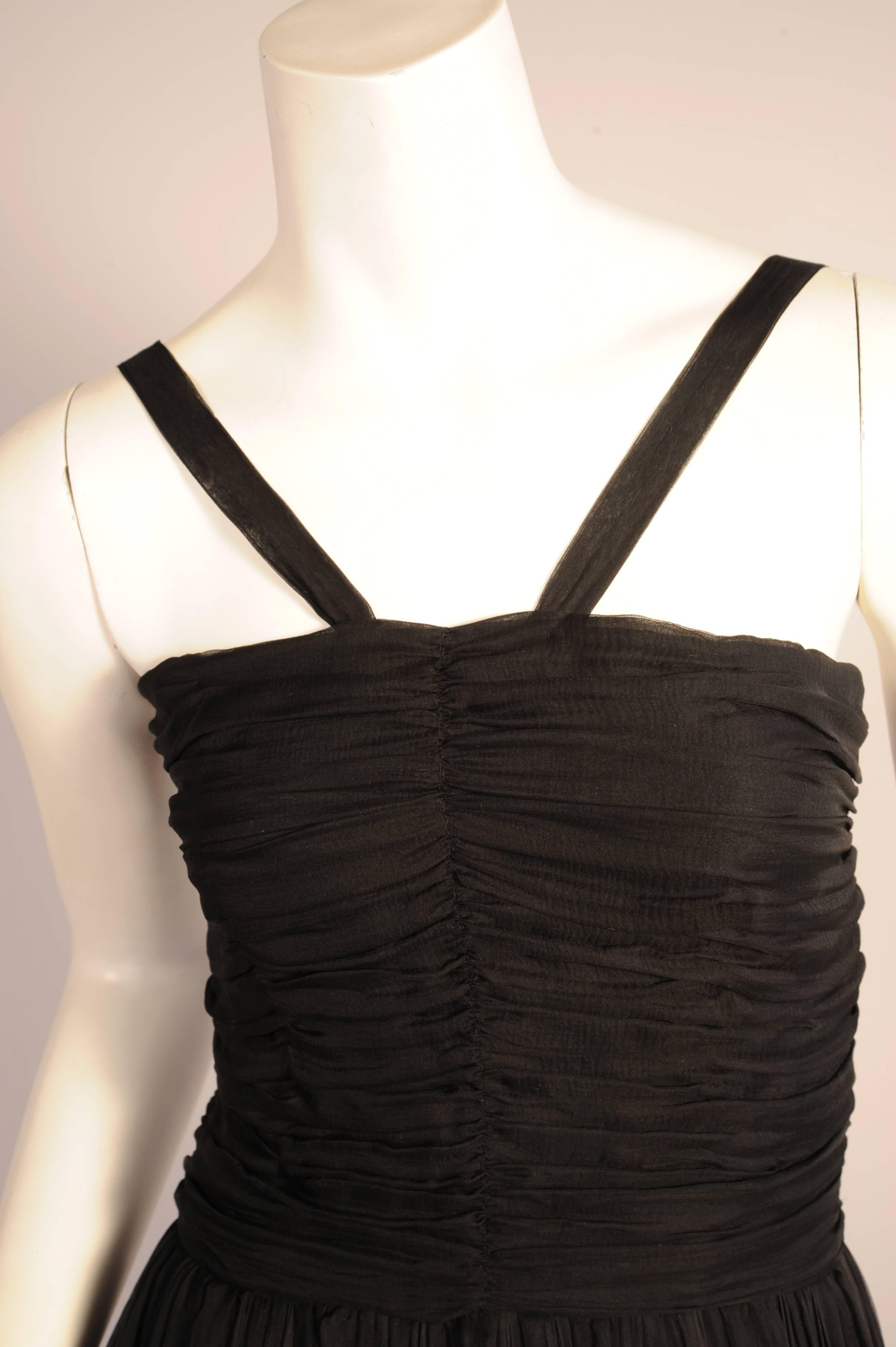 This beautiful Ben Reig black silk chiffon evening dress is reminiscent of the designs of Jean Desses. It has V shaped straps above a boned and horizontally gathered bodice. The full skirt is loosely pleated and gathered into the bodice. It falls