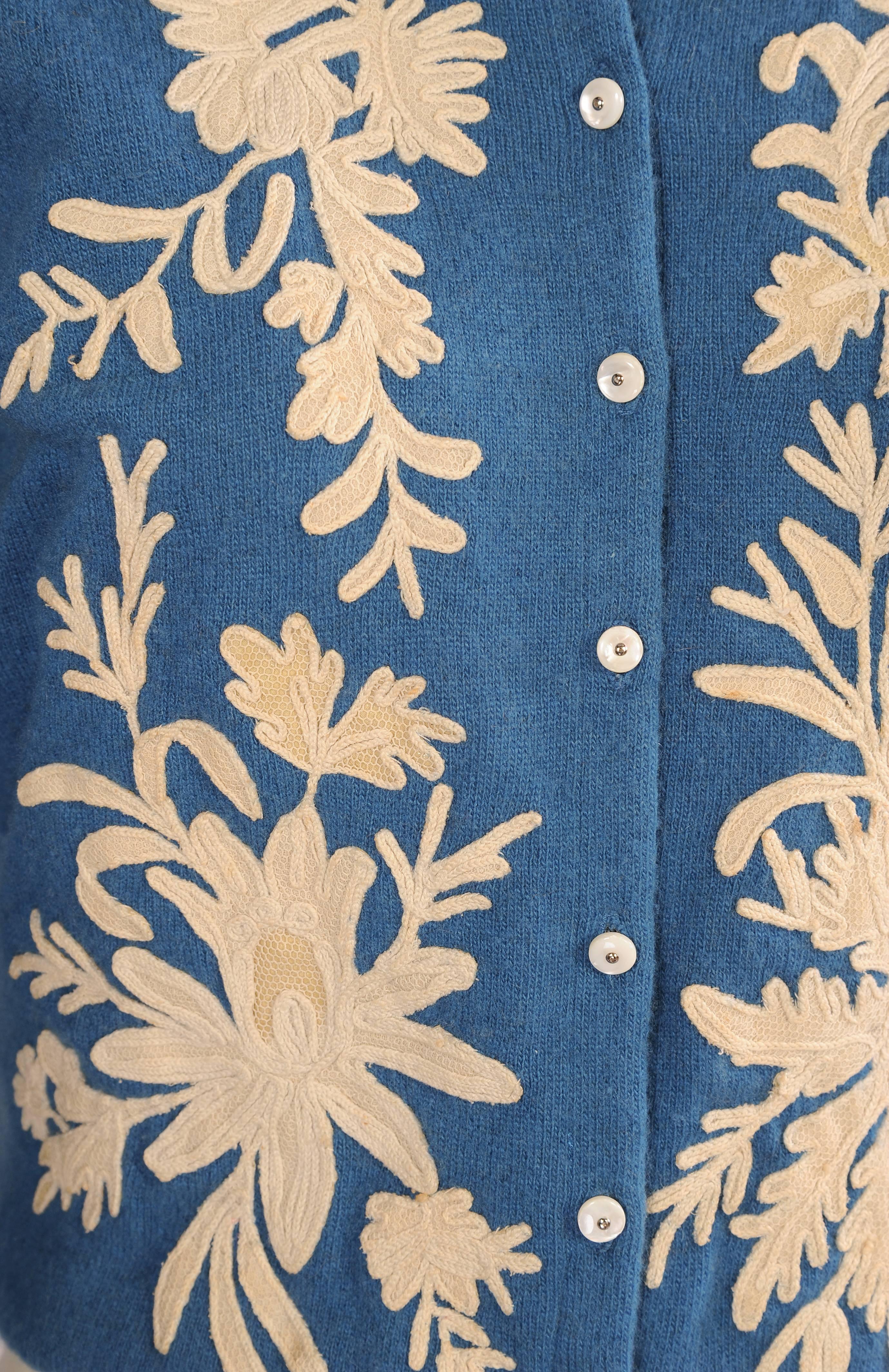 A French blue cashmere sweater is hand appliqued with creamy white antique lace in a floral design. Large lace motifs are hand sewn to either side of the sweater, both sleeves and the entire back. These appliques were carefully cut from antique