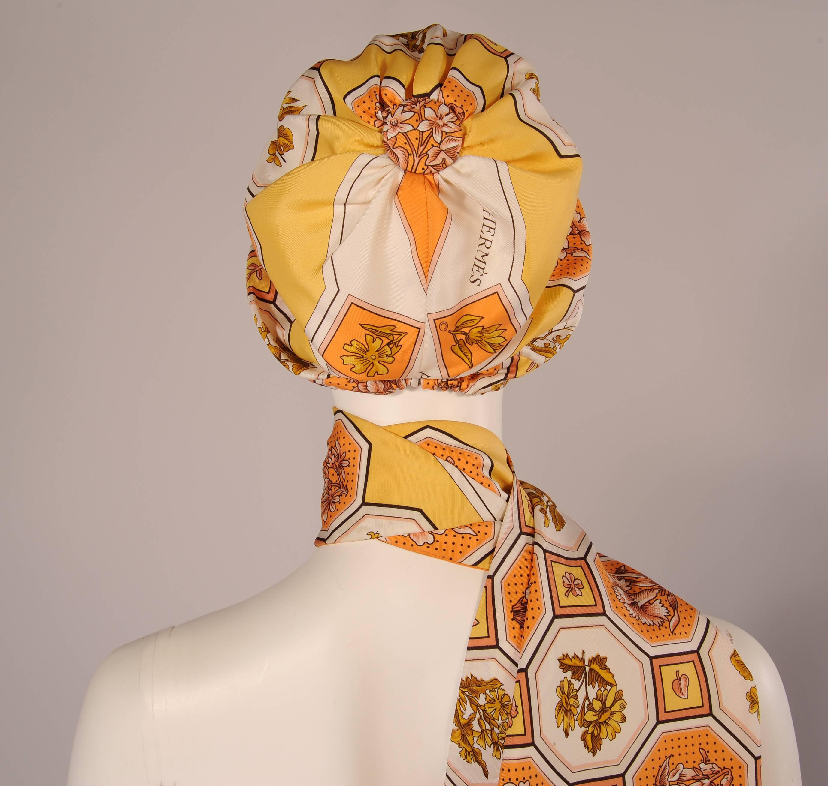 A charming floral print silk scarf from Hermes, Paris has been used for this matching hat and scarf. Shades of coral, peach, orange, yellow and gold pop against the white background. The hat is a turban style with a grosgrain ribbon band on the