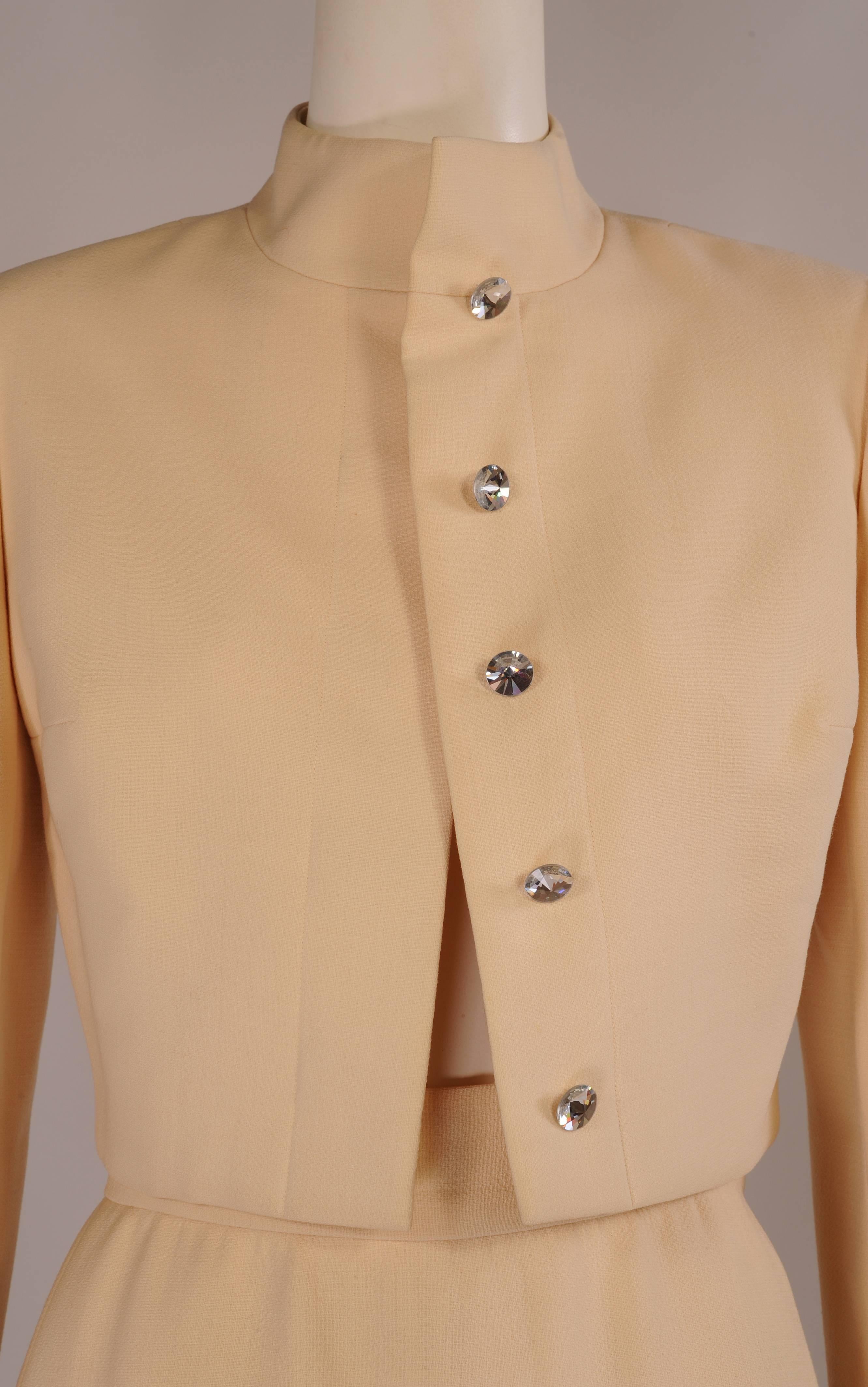 Chic and elegant, this cream wool crepe evening suit from Pauline Trigere has just the right amount of ornamentation.
The waist length jacket has a stand up collar and five large jeweled buttons for closure as well as one on each cuff. The matching