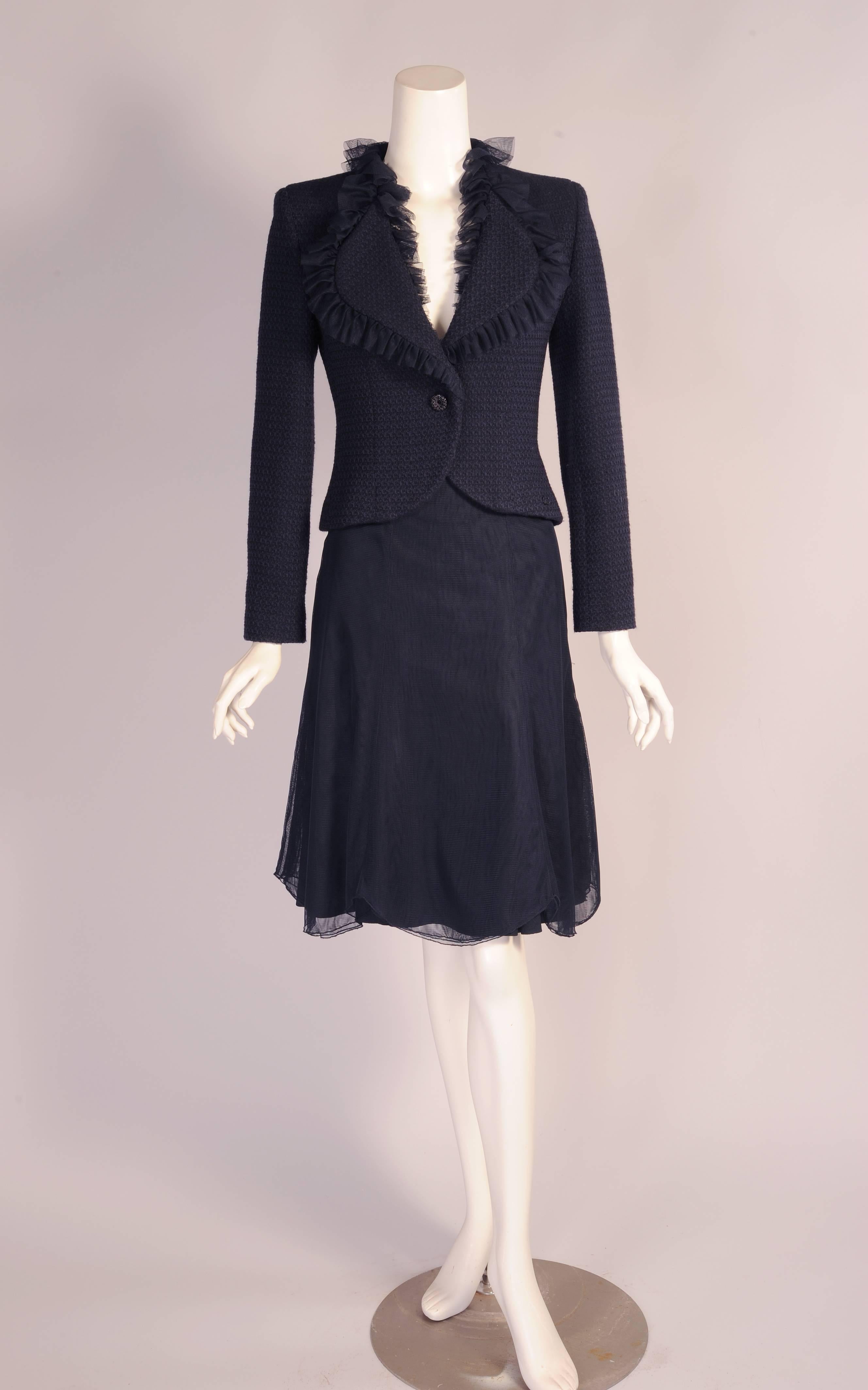 A truly feminine suit from Chanel is made from midnight blue tulle and tweed. The jacket has a tulle ruffle edged lapel and neckline. There is a jeweled button and double snap closure. It is lined in floral silk logo silk in midnight blue and edged