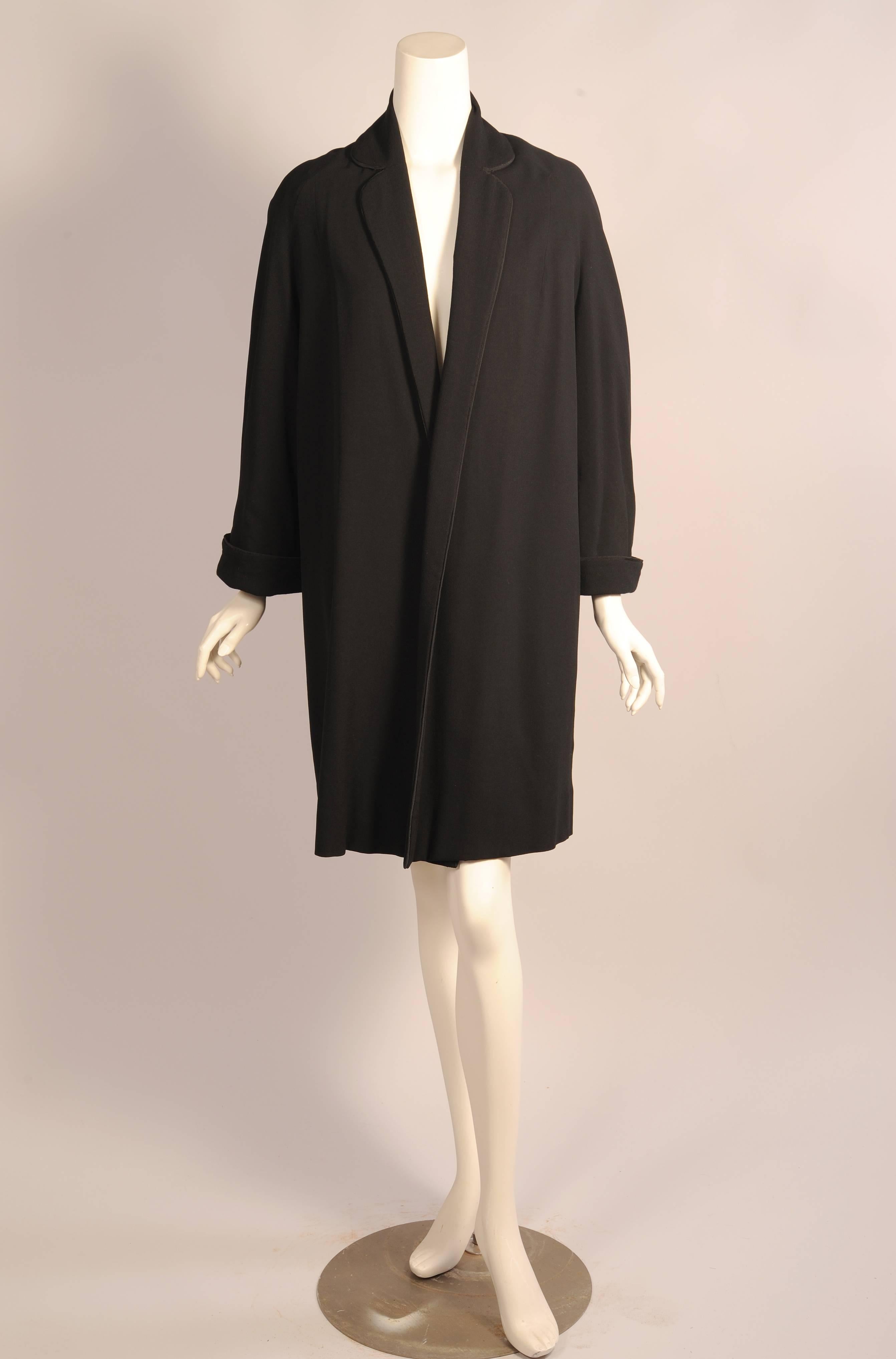 Leichte schwarze Wolle wird für diesen Duster- oder Swing-Mantel von Pierre Balmain Haute Couture verwendet. Der gekerbte Kragen reicht bei diesem verschlusslosen Mantel bis zum Saum. Der Kragen und die Manschetten sind mit schwarzem Soutache