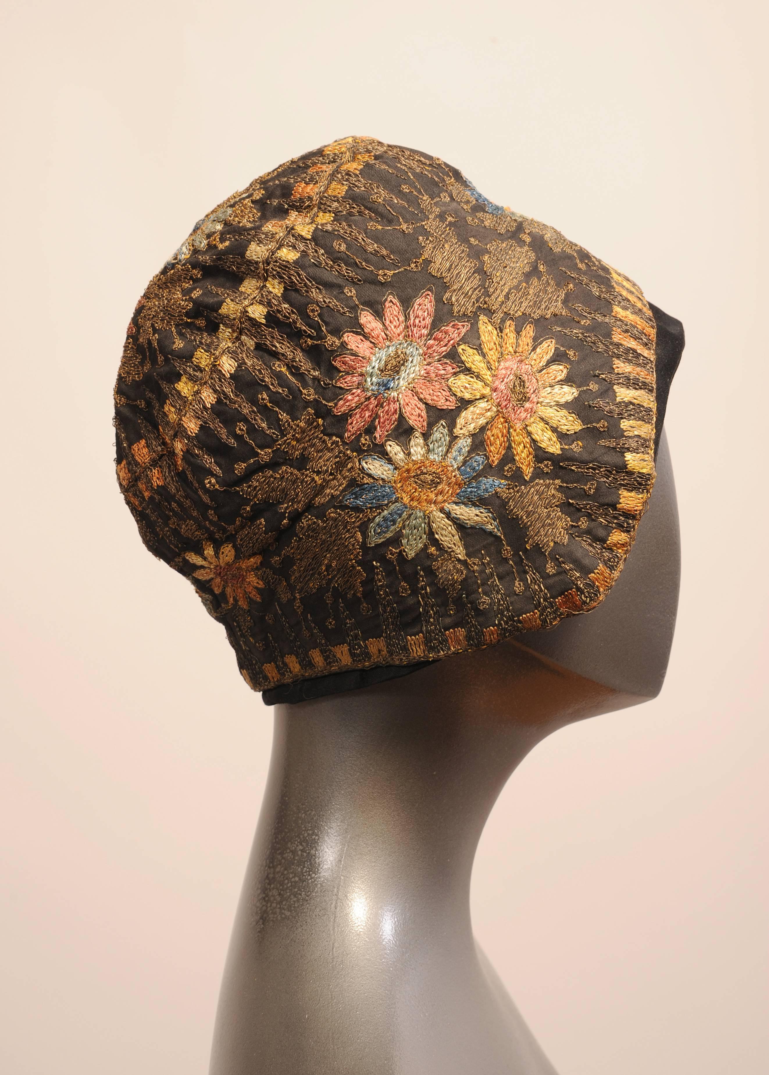 This 1920's black faille cloche has floral embroidery in shades of pink, blue and yellow that are combined with gold metallic thread embroidery. The hat also has two Art Deco borders worked in shades of yellow and peach with more gold metallic