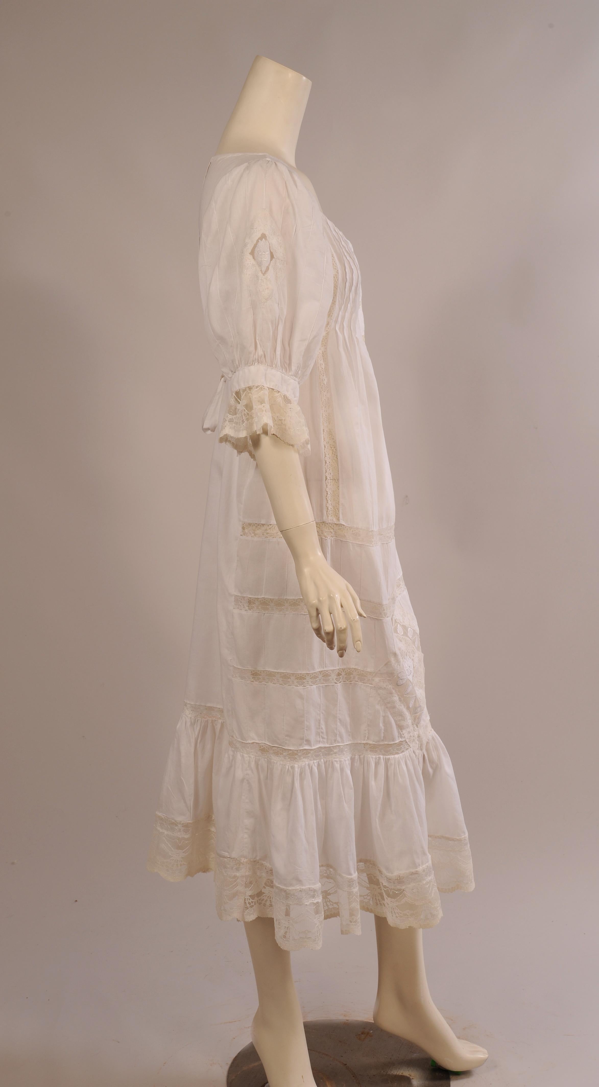 Perfect to wear right now and then again later while on winter vacation, this white cotton dress has a four button placket at the center front with pin tucks and lace insertion on either side.  There are ties below the bust that wrap around to the