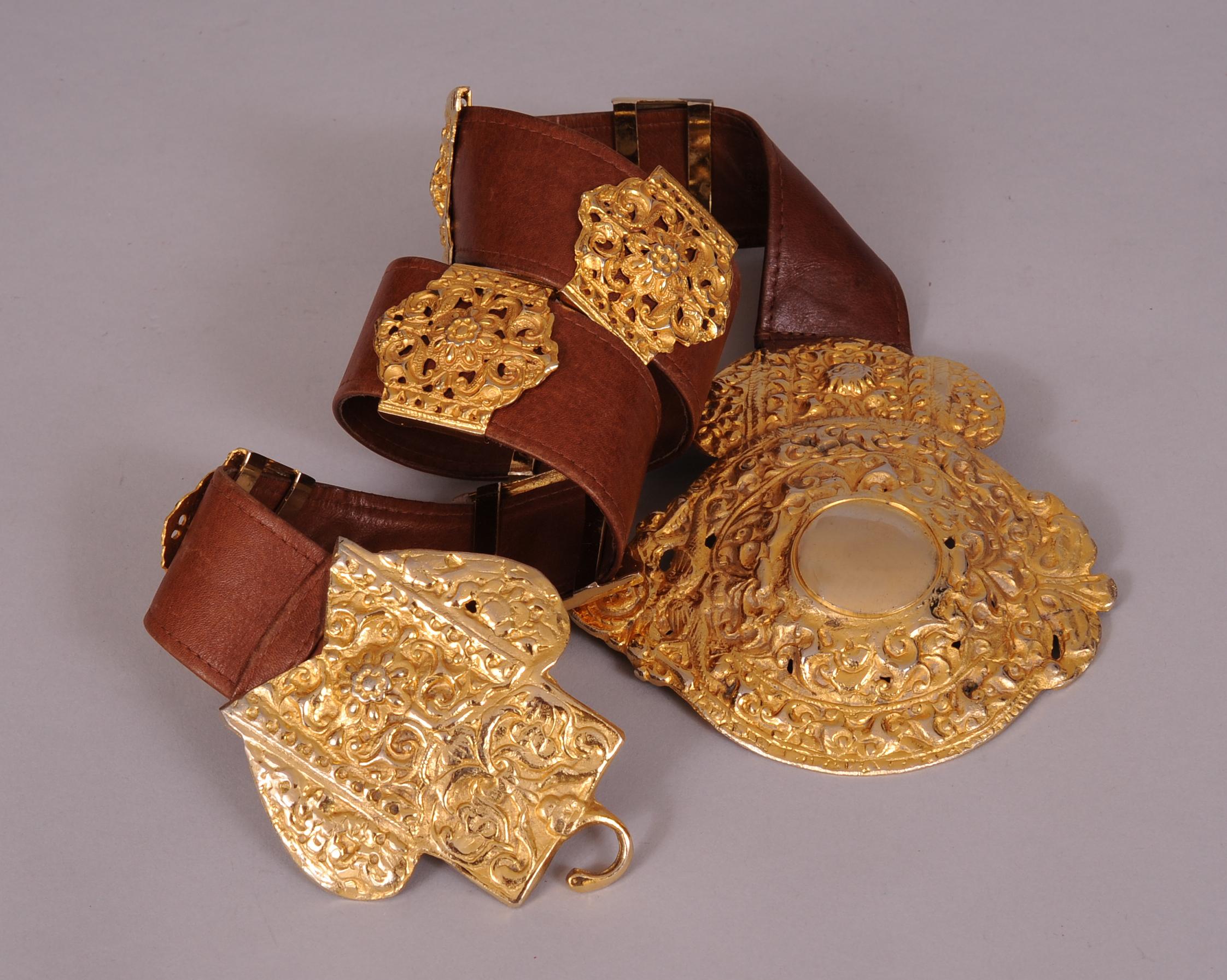 This supple brown leather belt is embellished with a large gold toned buckle and seven decorative slides in two different styles. The belt is stamped  Made in Italy by Roberta Di Camerino Expressly for Saks Fifth Ave. It is in excellent condition
