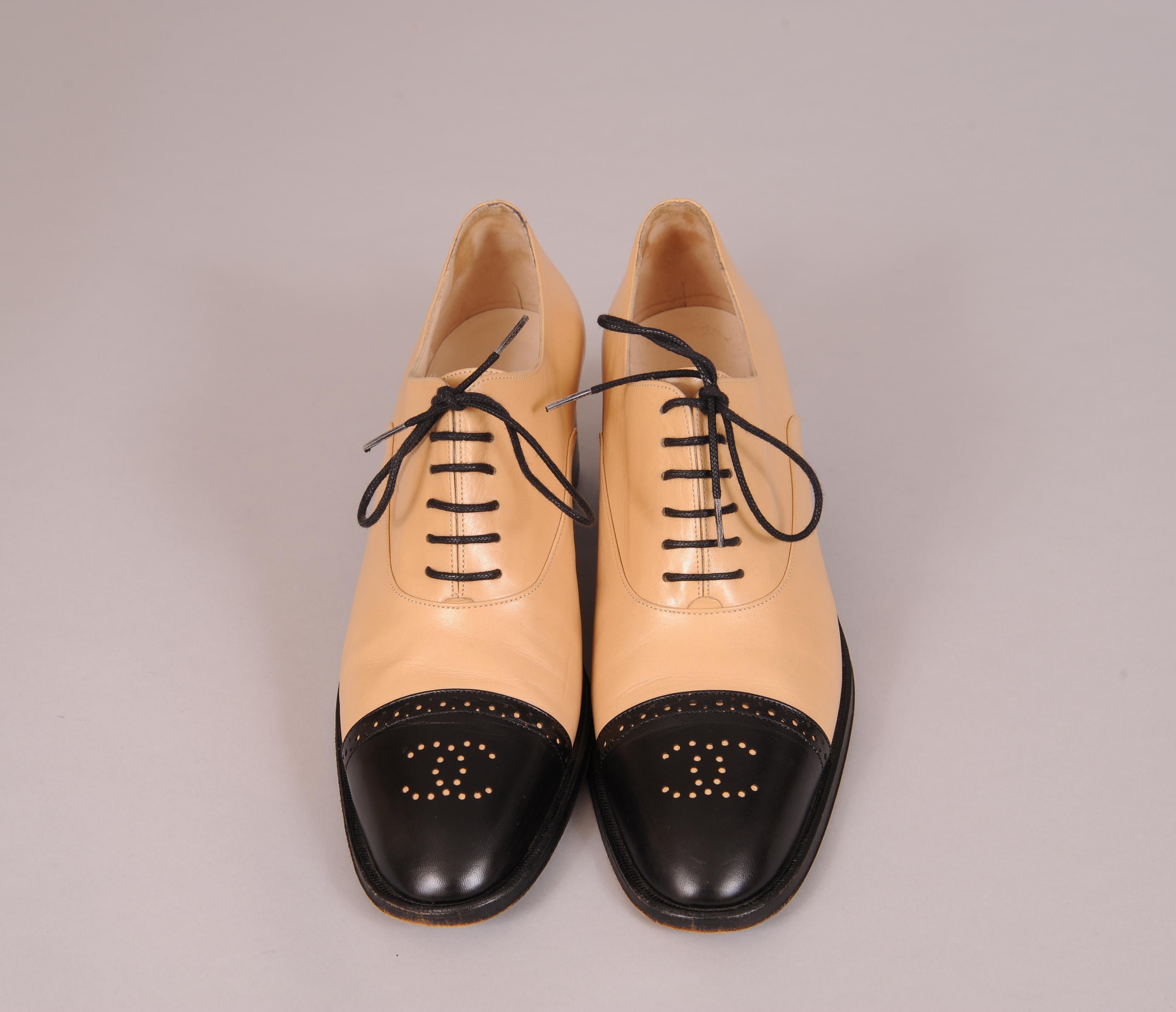 Tan leather oxfords are accented by black toe caps with the double C Chanel logo at the center. The shoes have black laces, heels and soles for added contrast. They appear to have been worn once or twice. The only wear is on the soles, the upper
