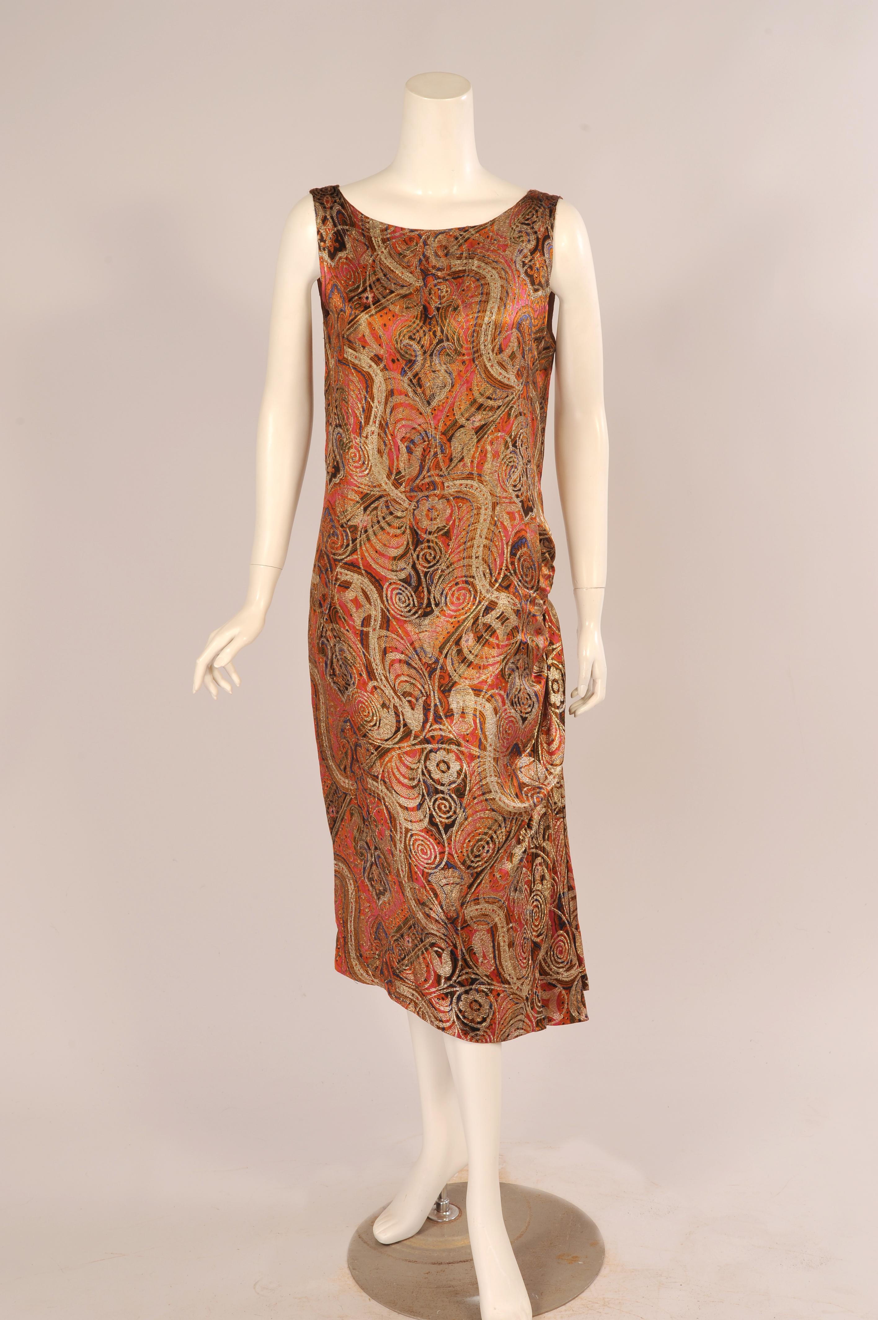 A rich multi-color silk paisley design is the background for a lustrous woven gold lame pattern swirling over the dress. It is sleeveless with a round neckline and a draped panel at the left side for added interest and movement. It is in excellent