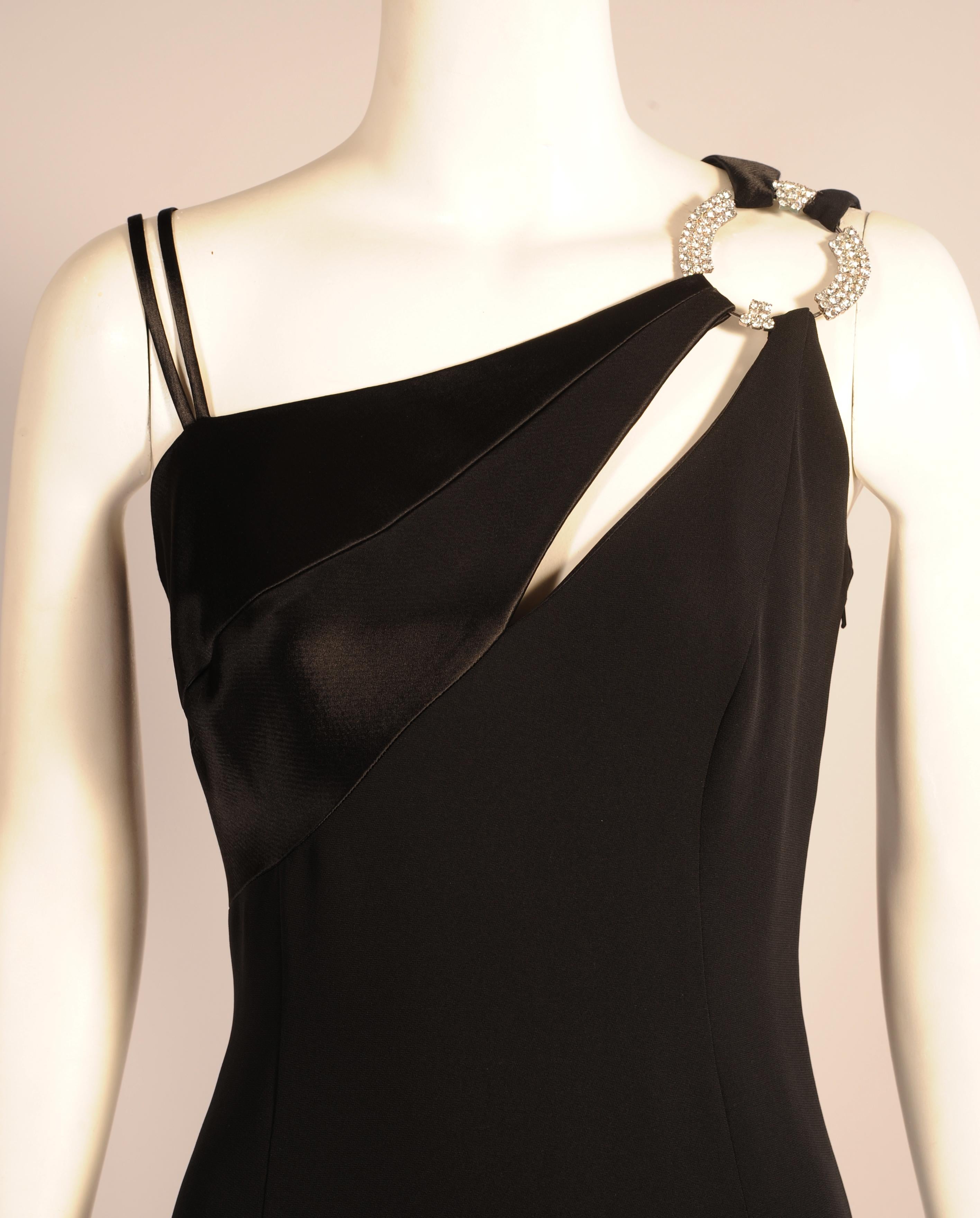 This sleek black silk crepe evening gown from the Milan based Italian designer Raffaella Curiel has an interesting neckline. There are two narrow strap on the right shoulder and a band of black silk satin which is fastened to a jewelled ornament on