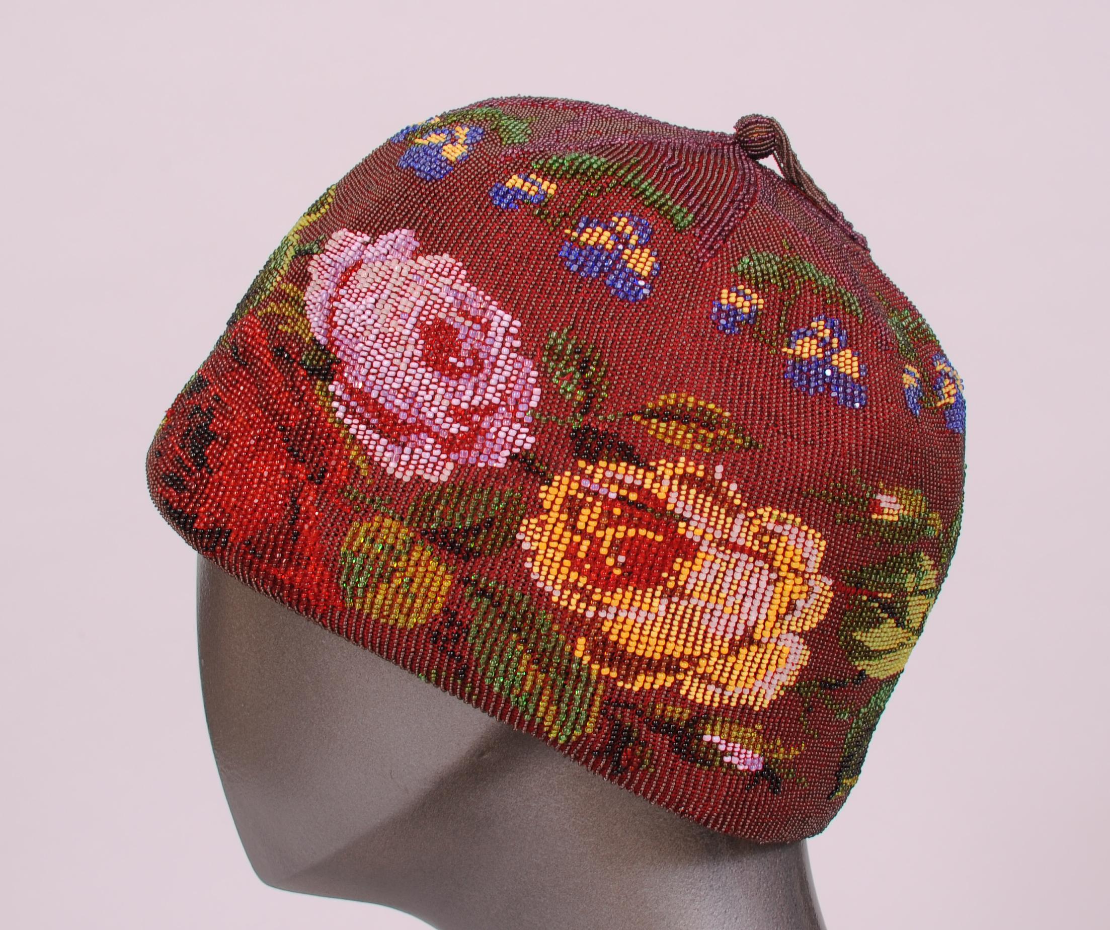 An amazing example of Victorian hand beadwork, this burgundy allover beaded hat has large flowers in pink, red and yellow with green leaves all around the edge. Smaller blue and yellow flowers with green leaves surround the top. It is completed by a
