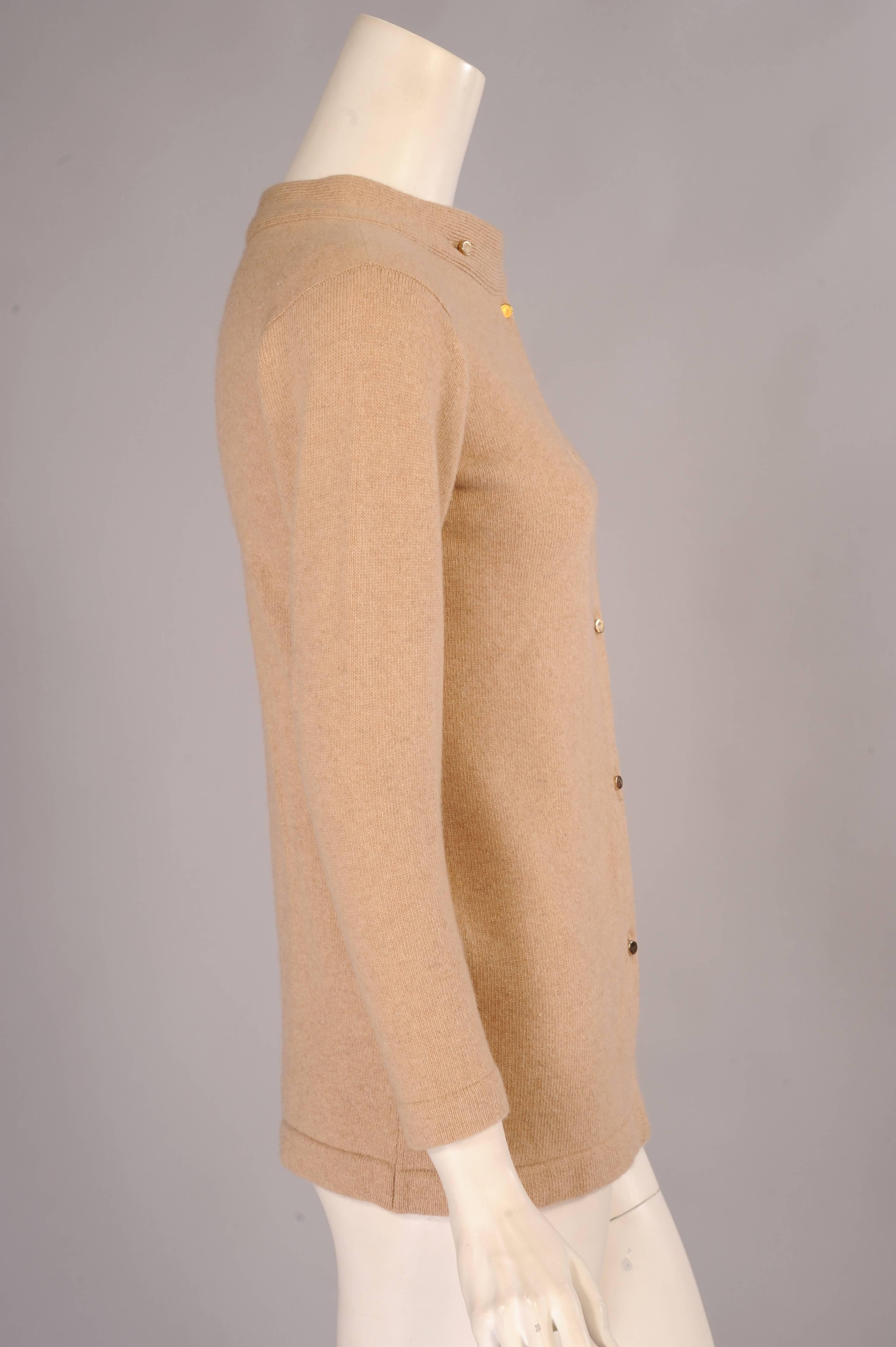 Natural Scottish Cashmere in at least a 4 ply thickness is used for this cardigan sweater from Bonnie Cashin. The long straight shape has a distinctive treatment at the neckline. The sweater has a stand up collar and two small gold toned buttons