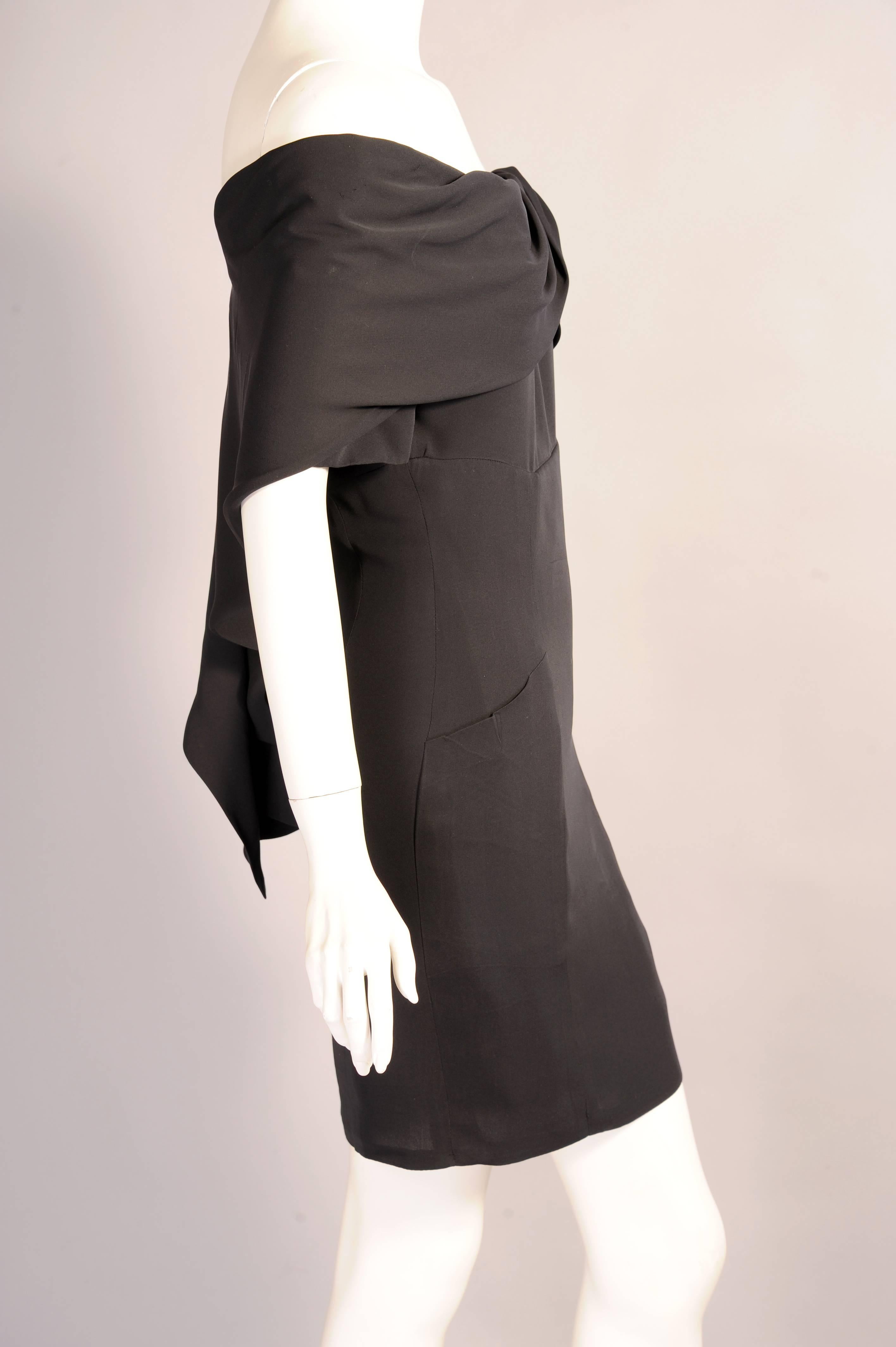 This sexy black silk cocktail dress from Chanel has an interesting draped off the shoulder neckline which cascades down the back of the dress. The dress has short sleeves, two pockets, a center back zipper and the drape closes with a hook and eye.