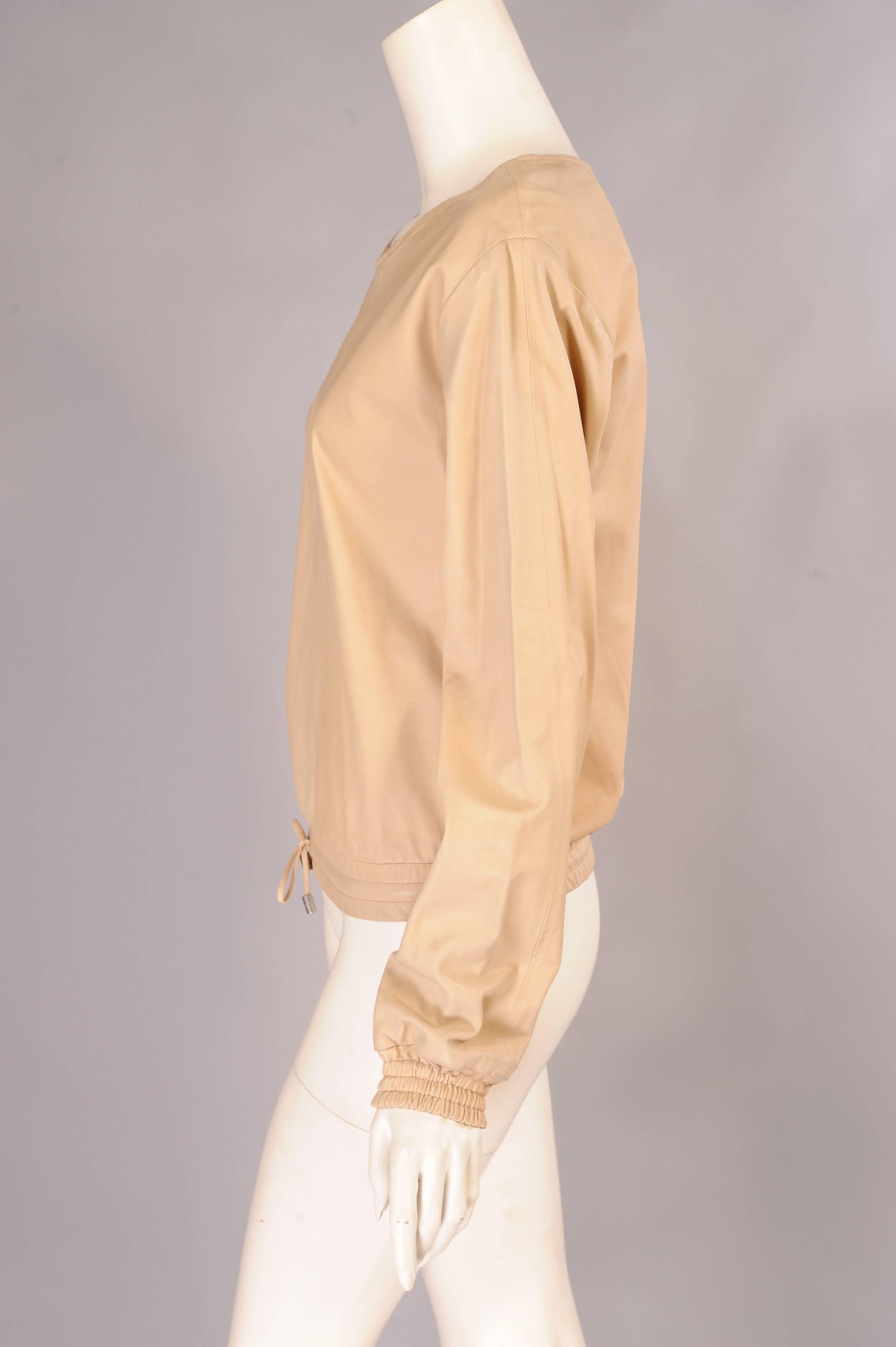 Designed like a sweatshirt this pale beige calfskin pullover top from the Chanel Boutique line is accented with elasticized cuffs and waistband. The waist also has a drawstring with silver toned metal tips bearing the Chanel logo. This piece is in
