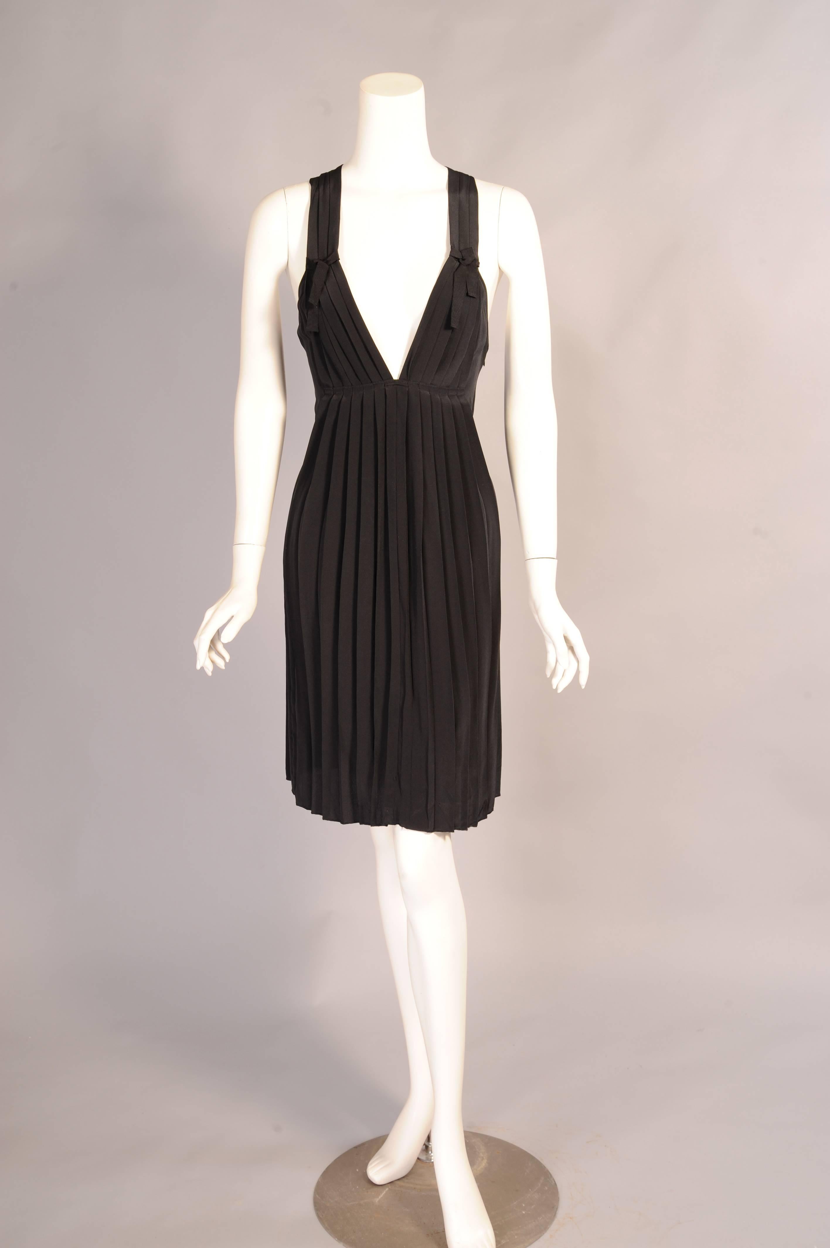 A plunging neckline and Empire waist define the shape of this pleated silk dress. The straps have a decorative gros grain ribbon and bow and they fall into a racer back. There is a left side zipper and a gros grain ribbon belt. The dress has never