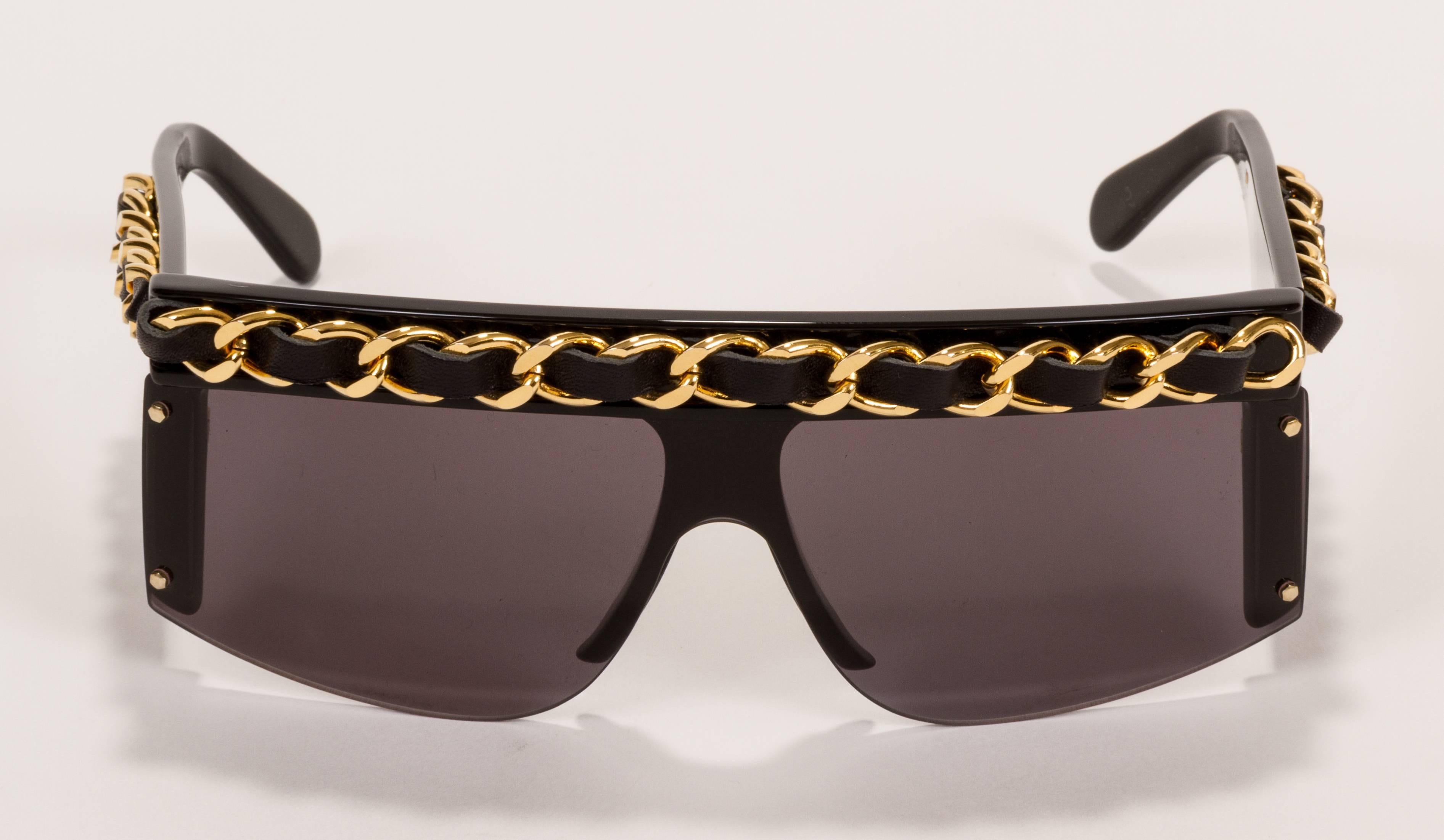 1980s Chanel black oversize celluloid sunglasses with gold-plated chain interlaced with black lambskin on top and sides. Comes with Chanel leather case and box. Minor scratches on frame and lenses.