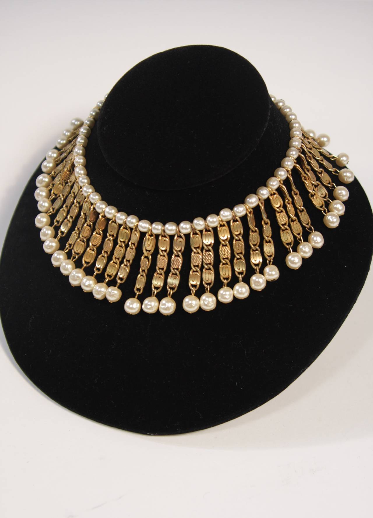 This Miriam Haskell chic bib style choker is composed of gold toned metal linked swirls and faux pearl accents. Features an adjustable length closure and is signed,
Miriam Haskell 

Measures (Approximately)
Length: 12