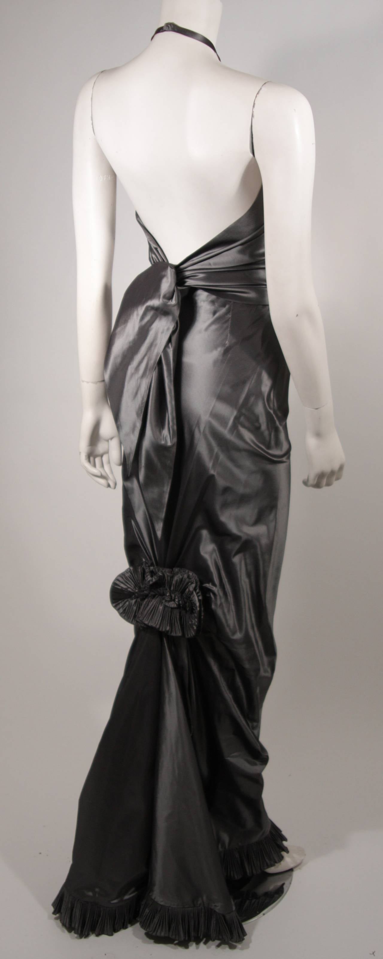 This stunning Oscar De La Renta evening ensemble is composed of a beautiful silver metallic fabric. The halter top has an over sized tie detail. The skirt features a slim cut which is accentuated at the knee by a floral ruffle that culminates into a